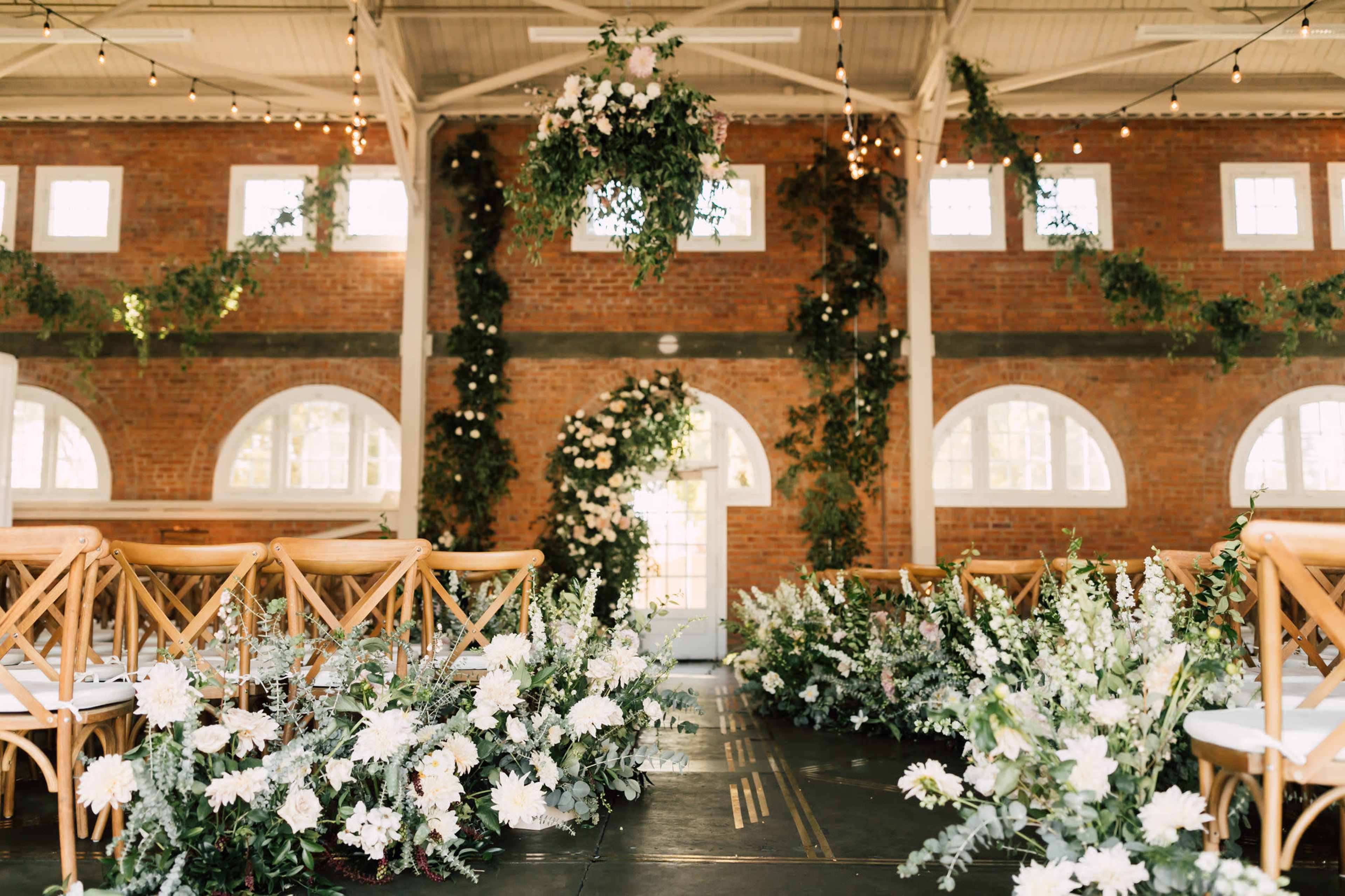 A decorated indoor venue with brick walls, adorned with hanging greenery and floral arrangements, set up for a wedding ceremony.