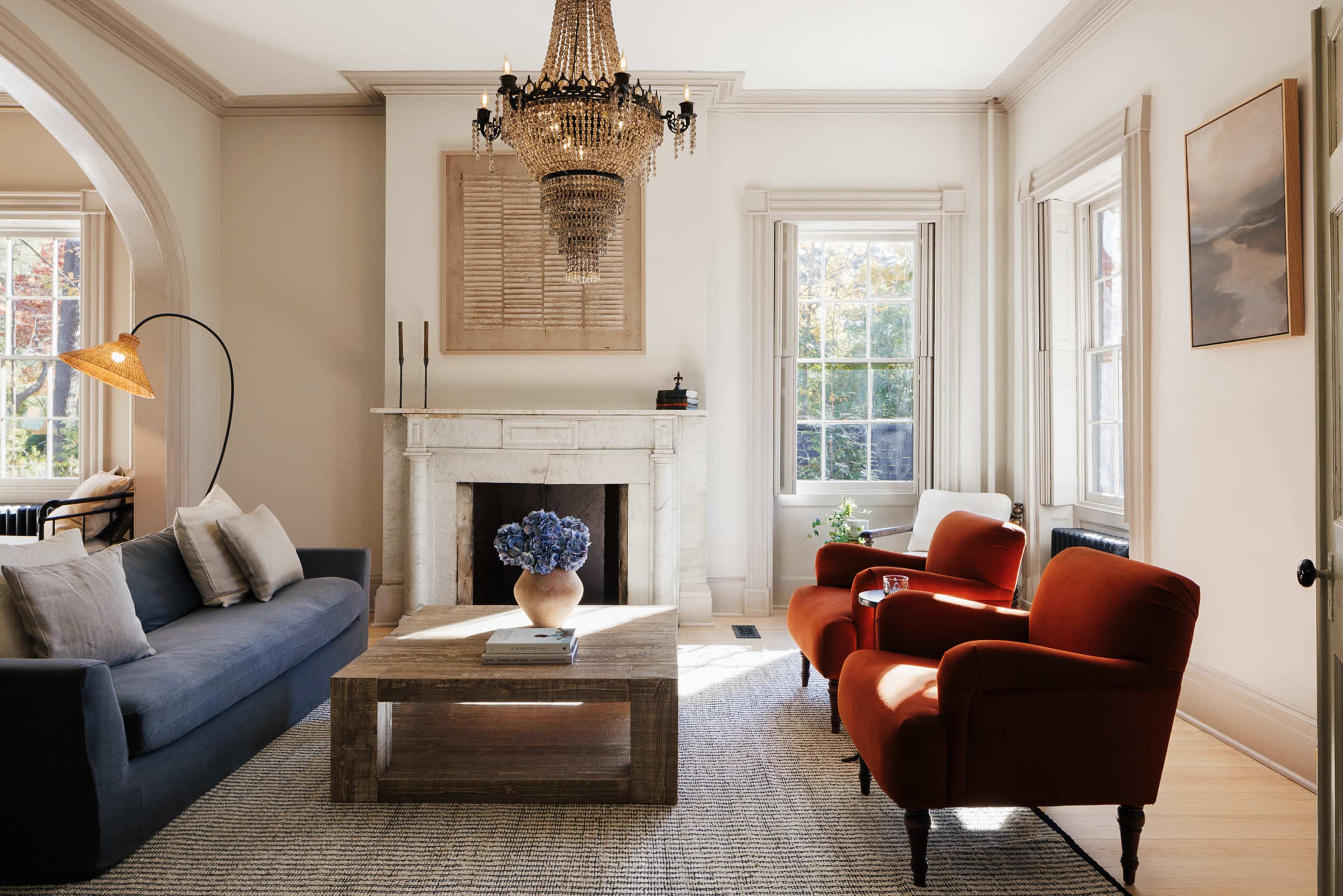 The living room features a blue sofa, two red armchairs, a wood coffee table, and a chandelier above a stone fireplace.