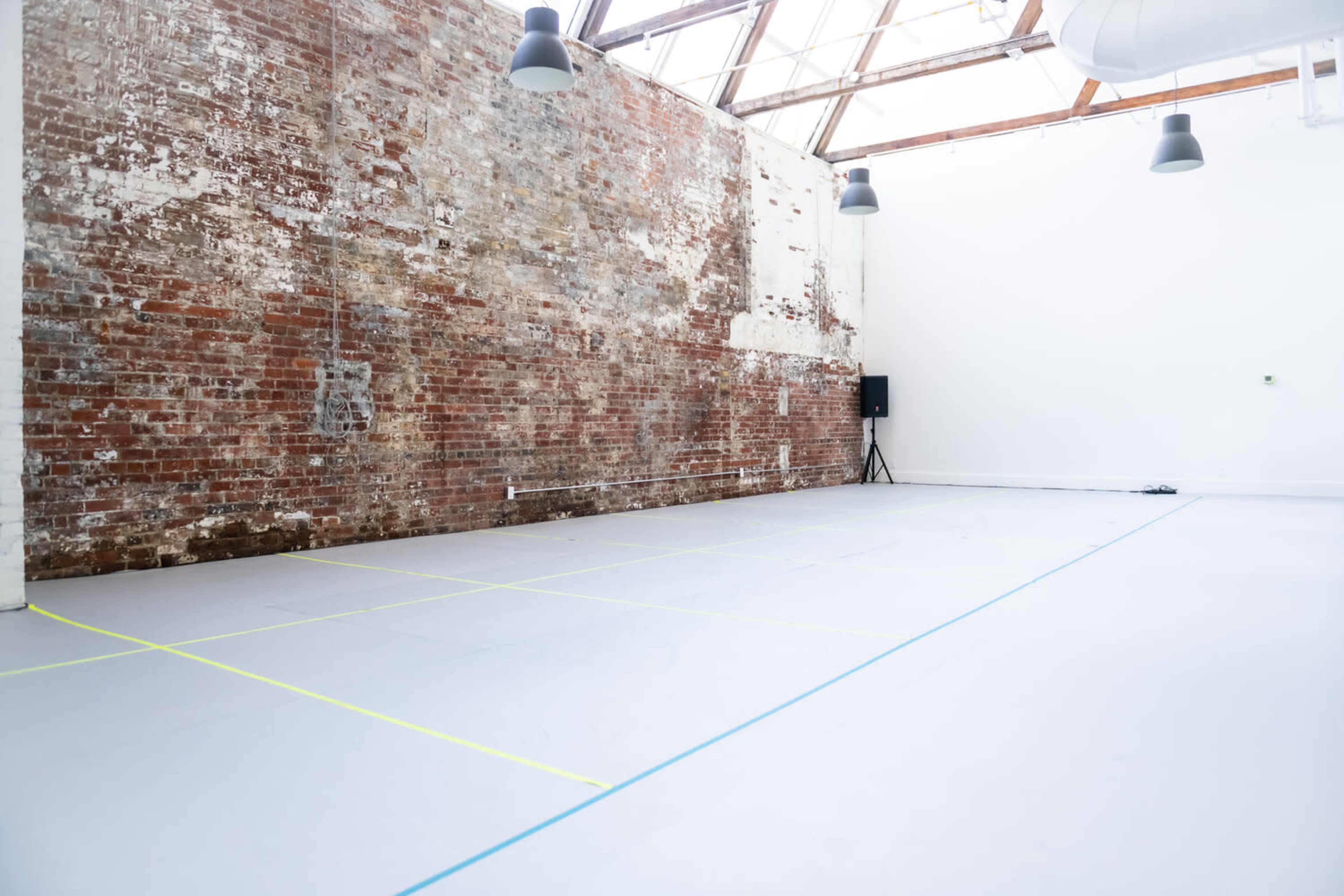 An empty studio space with a large, textured brick wall and a light gray floor marked with colored lines.