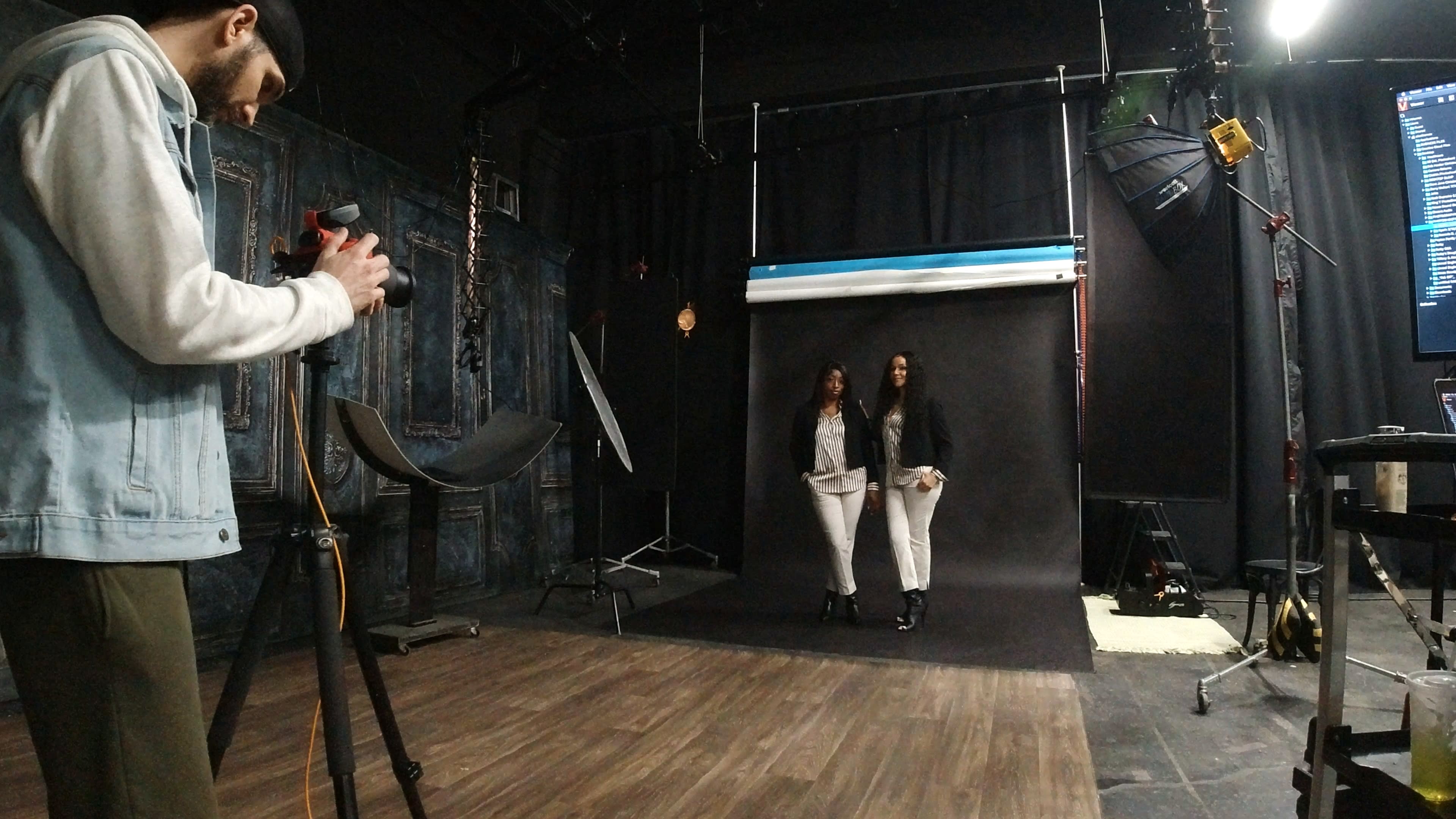 A photographer captures a studio session with two women posing in front of a black backdrop.