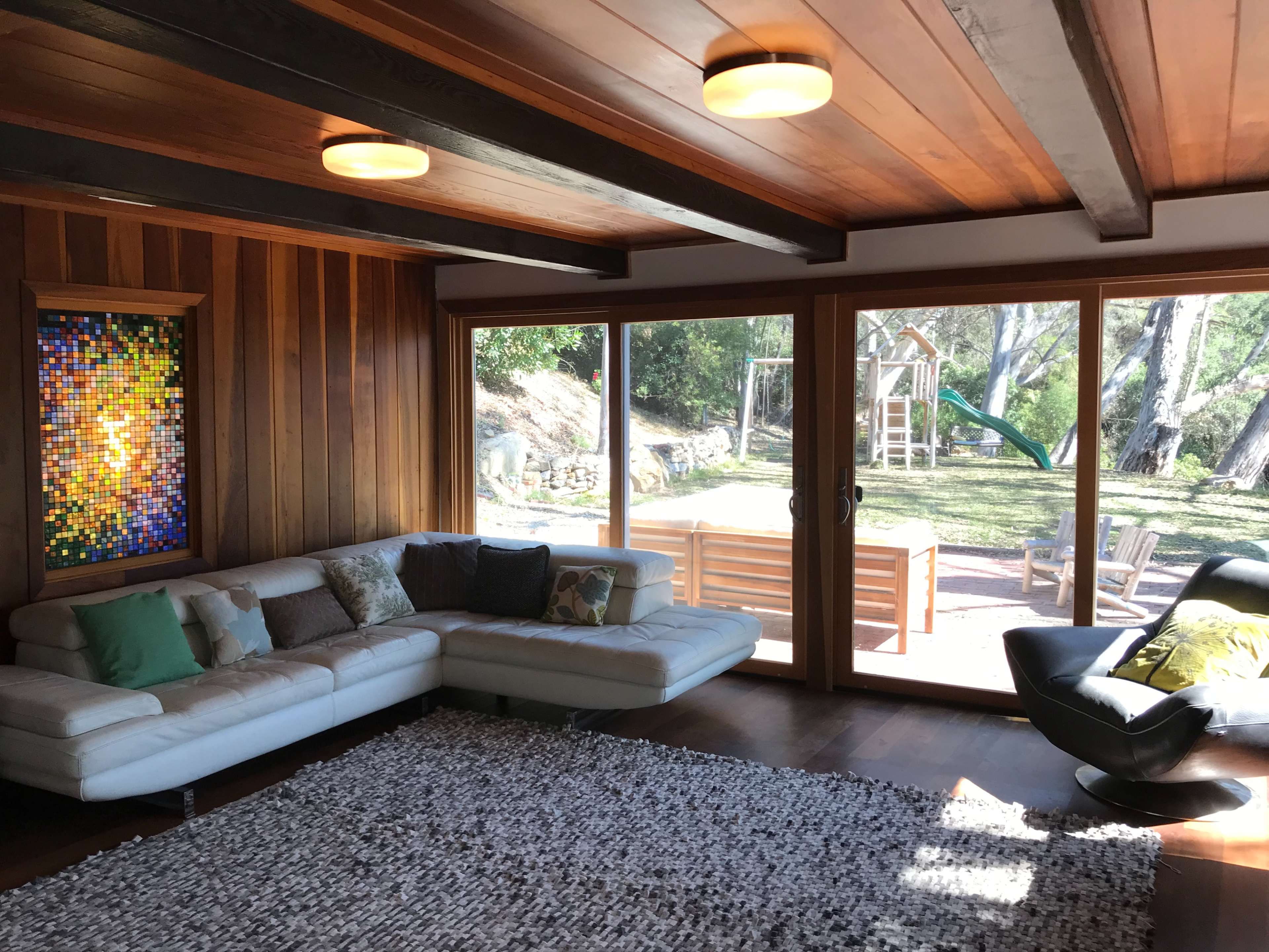 A modern living room features a white sectional sofa and large sliding glass doors that open to a backyard playground.