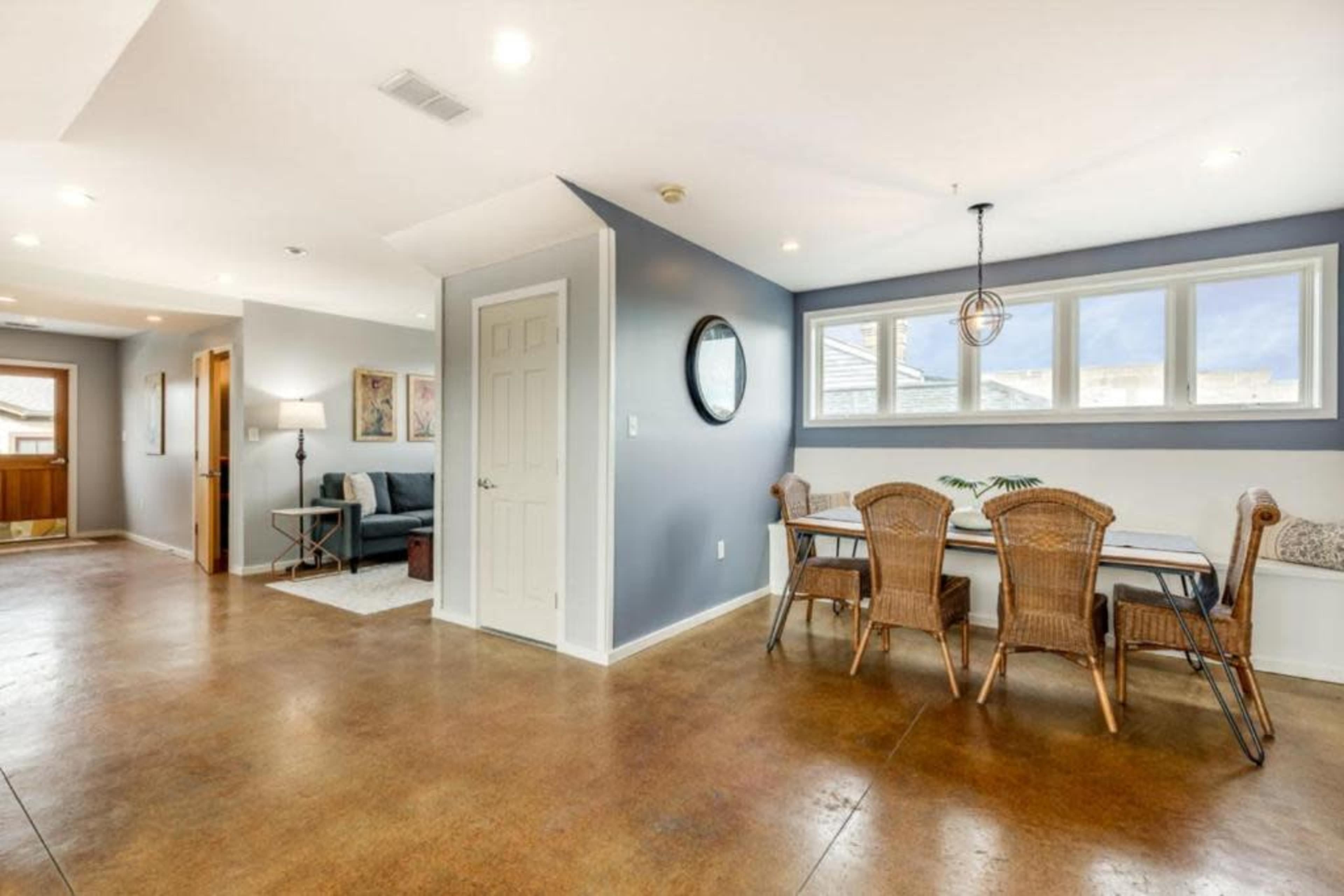 The image shows a modern living space featuring a dining area with a table and chairs, a seating area with a sofa, and large windows providing natural light.
