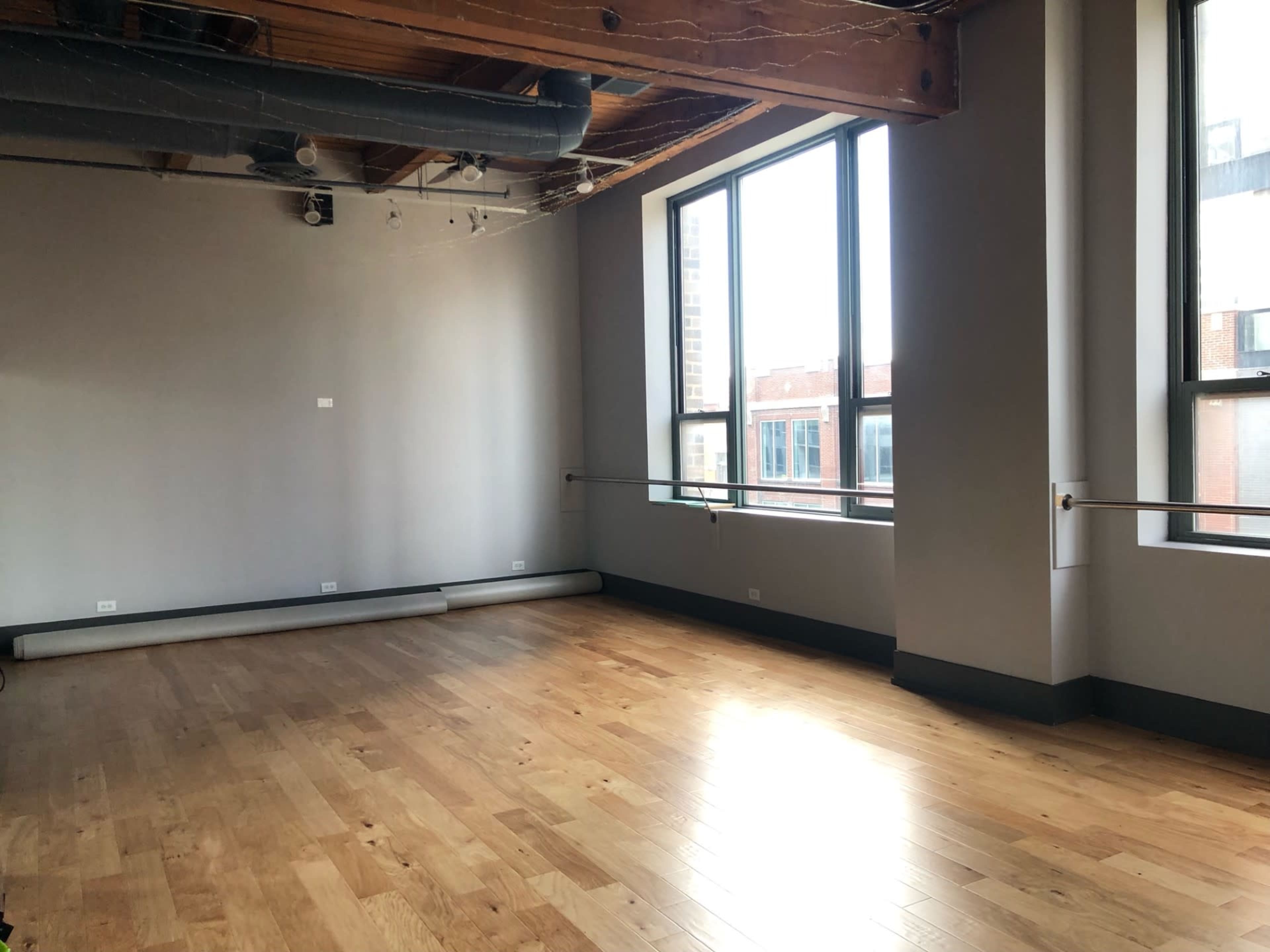 An empty room with large windows, wooden floors, and exposed beam ceilings.