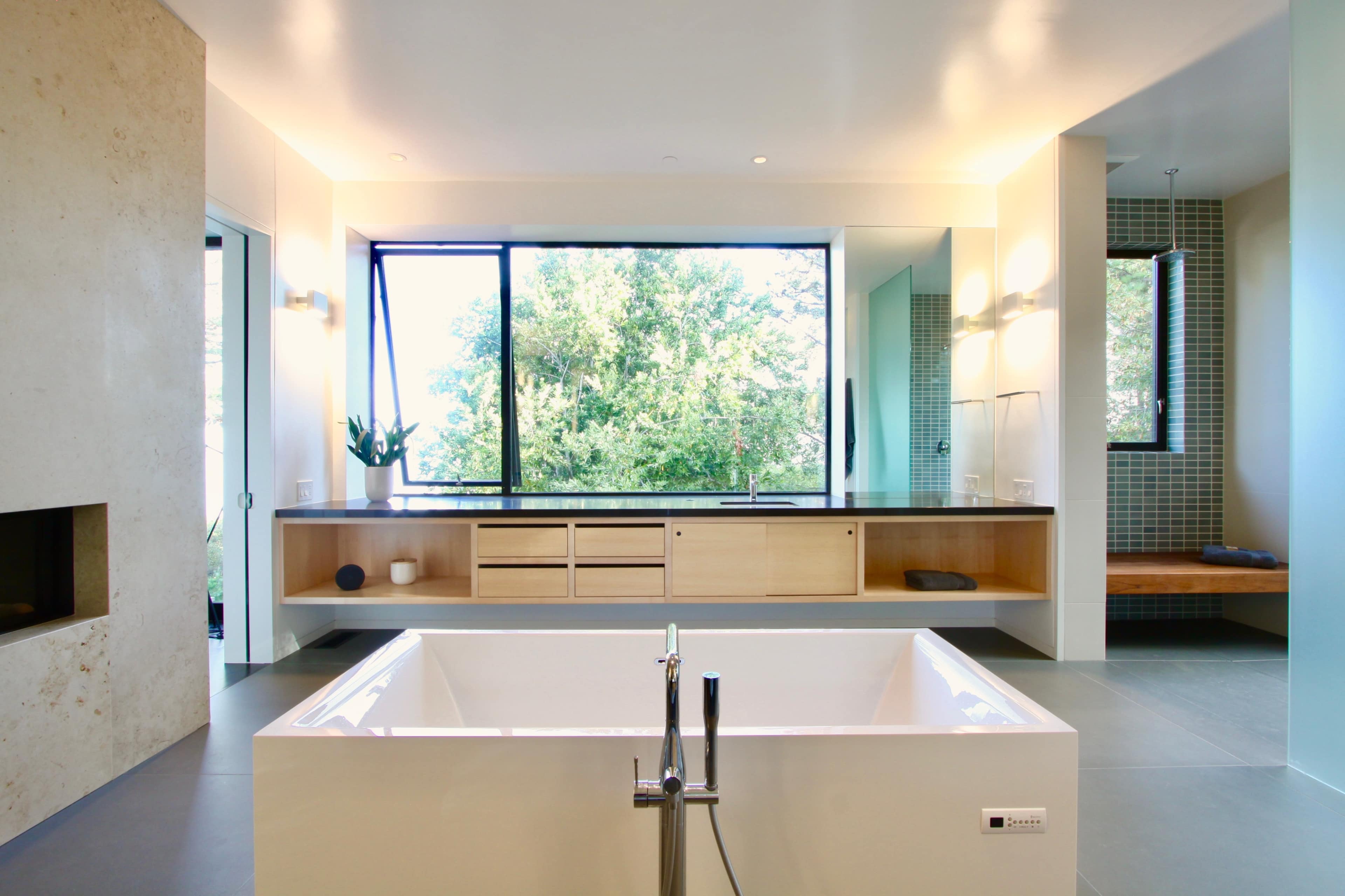 The bathroom features a freestanding bathtub in front of a large window overlooking greenery, with a modern wooden cabinet and wall panels.