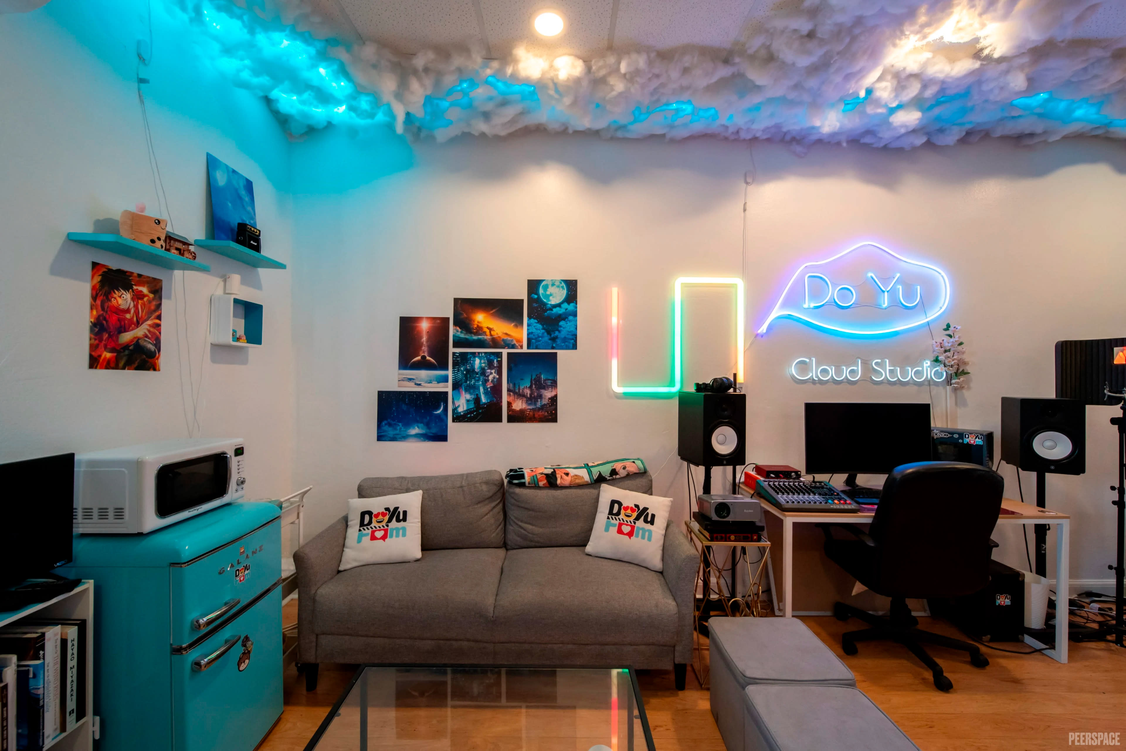 The image shows a creatively designed studio space with a couch, colorful lighting, and various art pieces on the walls, including a workspace with audio equipment.