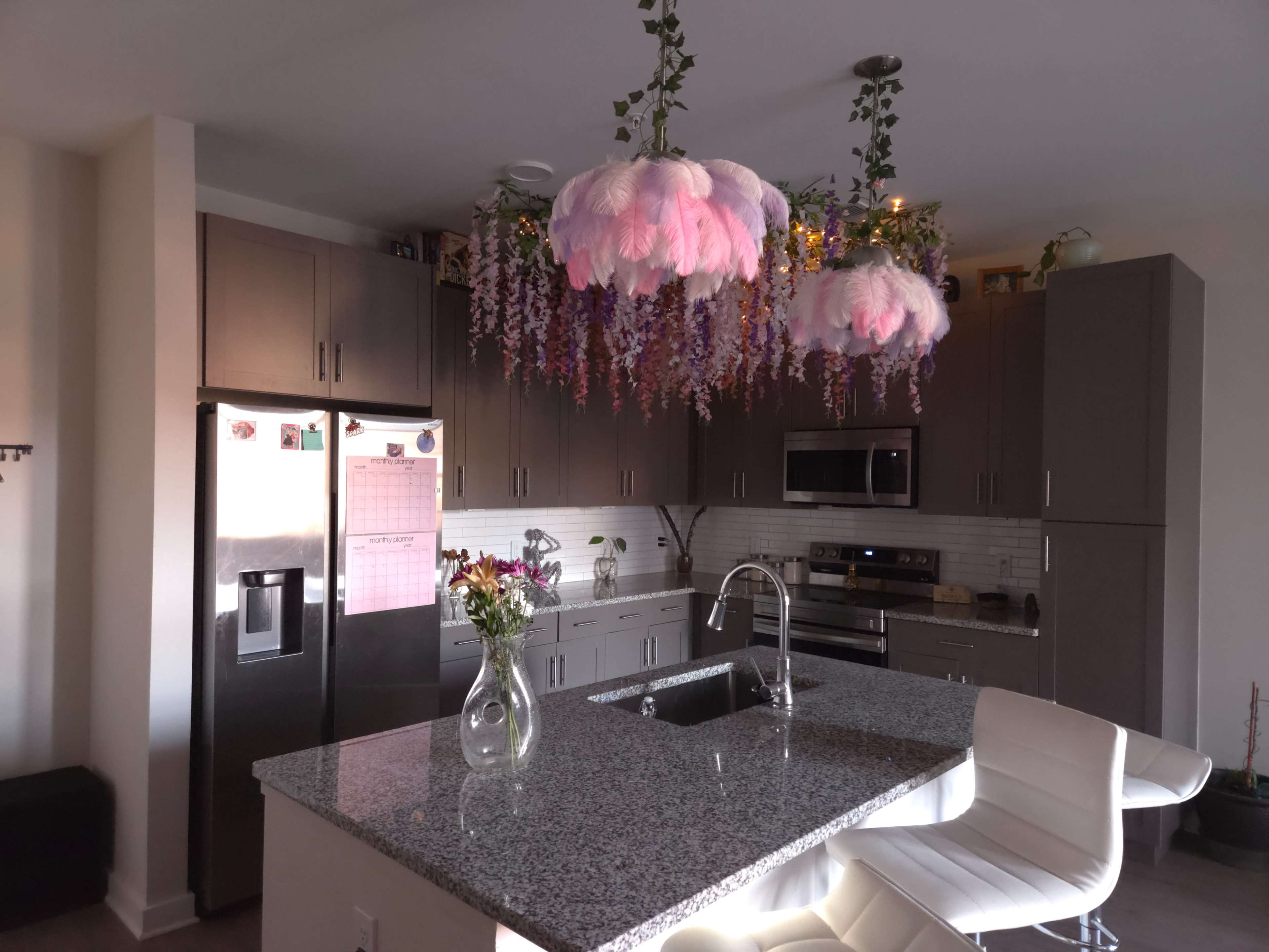 The kitchen features modern gray cabinetry, a central island with a sink, and decorative pendant lights adorned with floral arrangements.