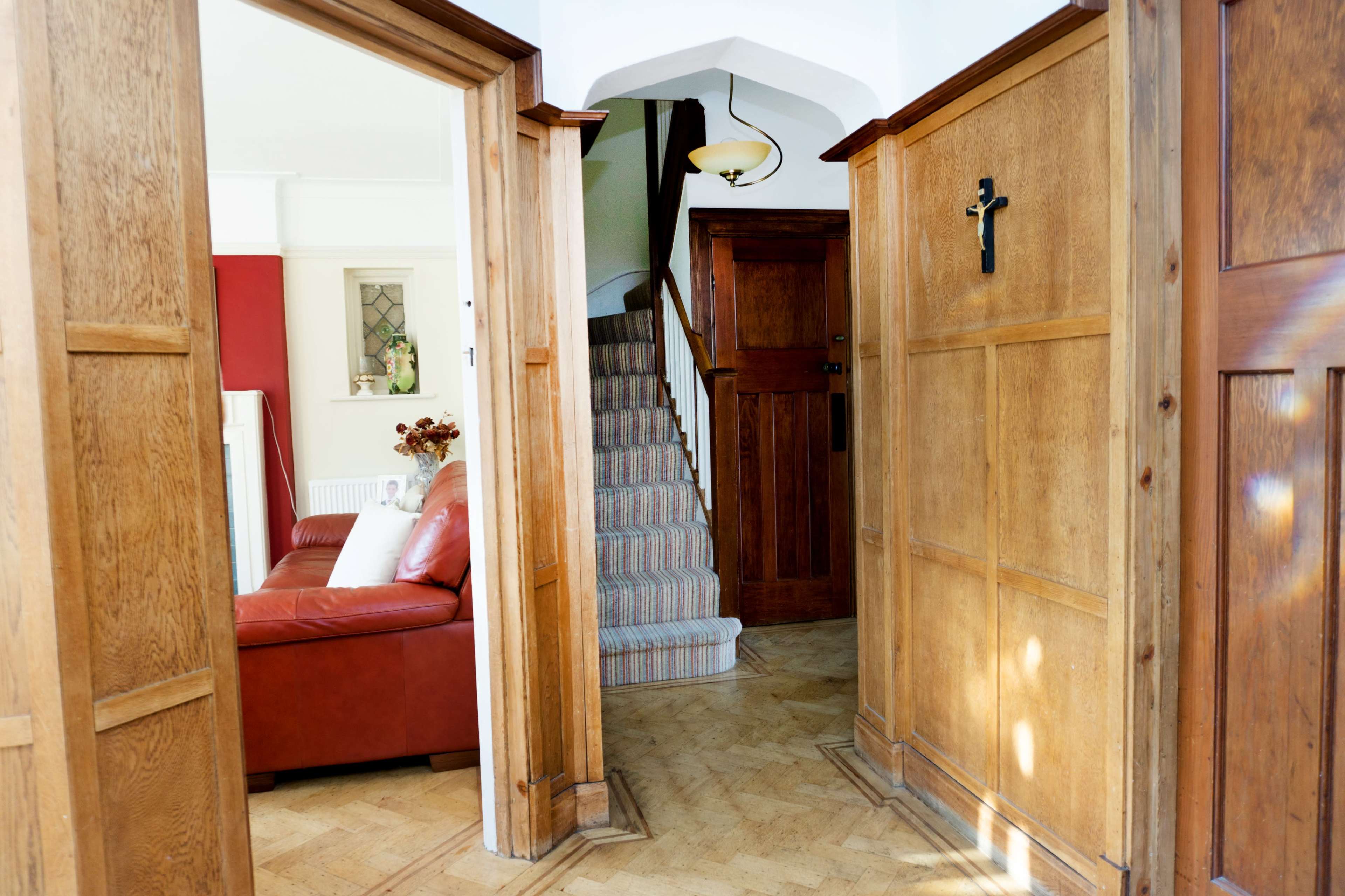 A hallway leading to a staircase, with wooden walls and a red living room visible on one side.