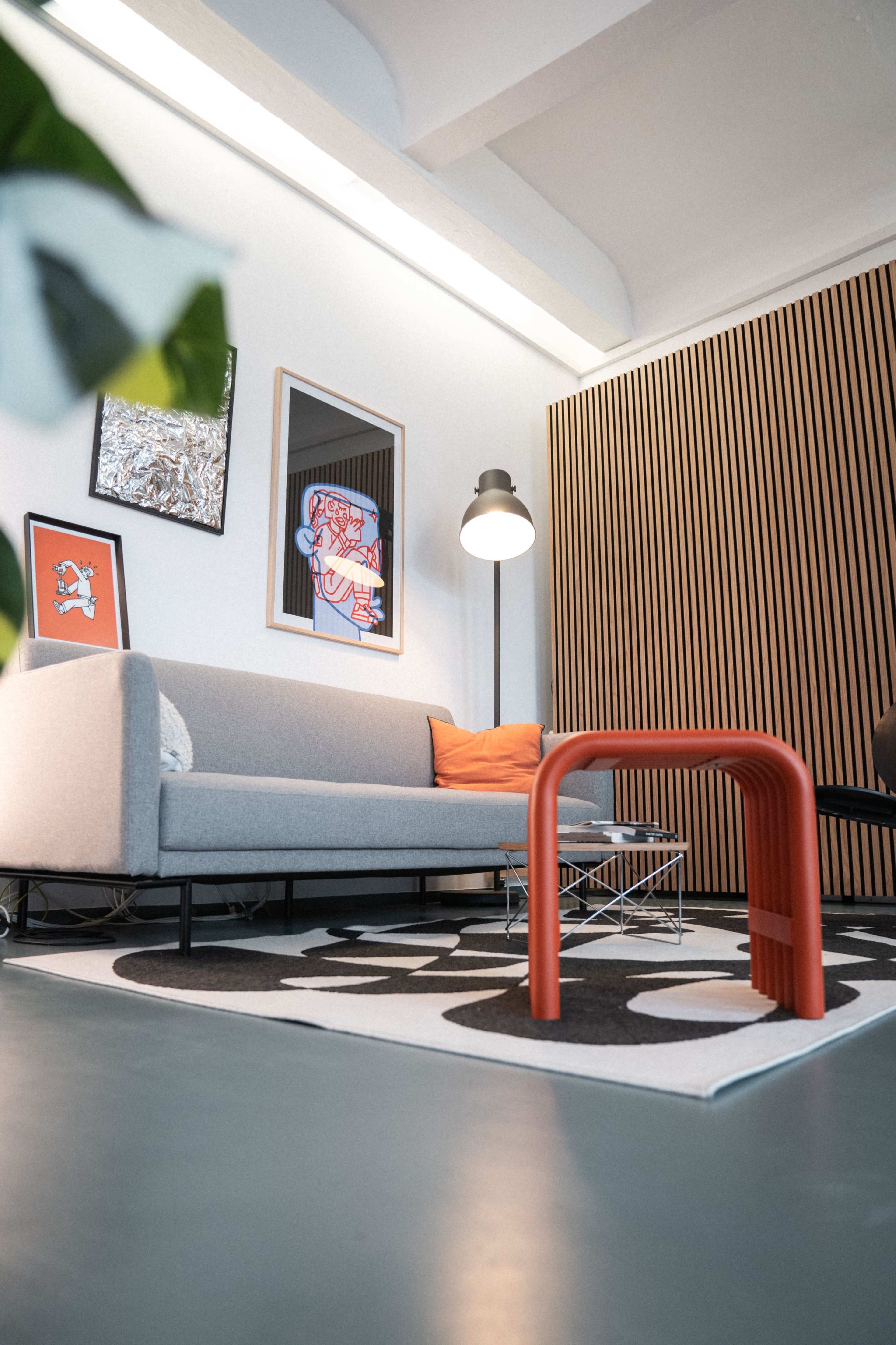 A modern living room with a gray sofa, an orange accent pillow, and a large patterned rug on a sleek floor.