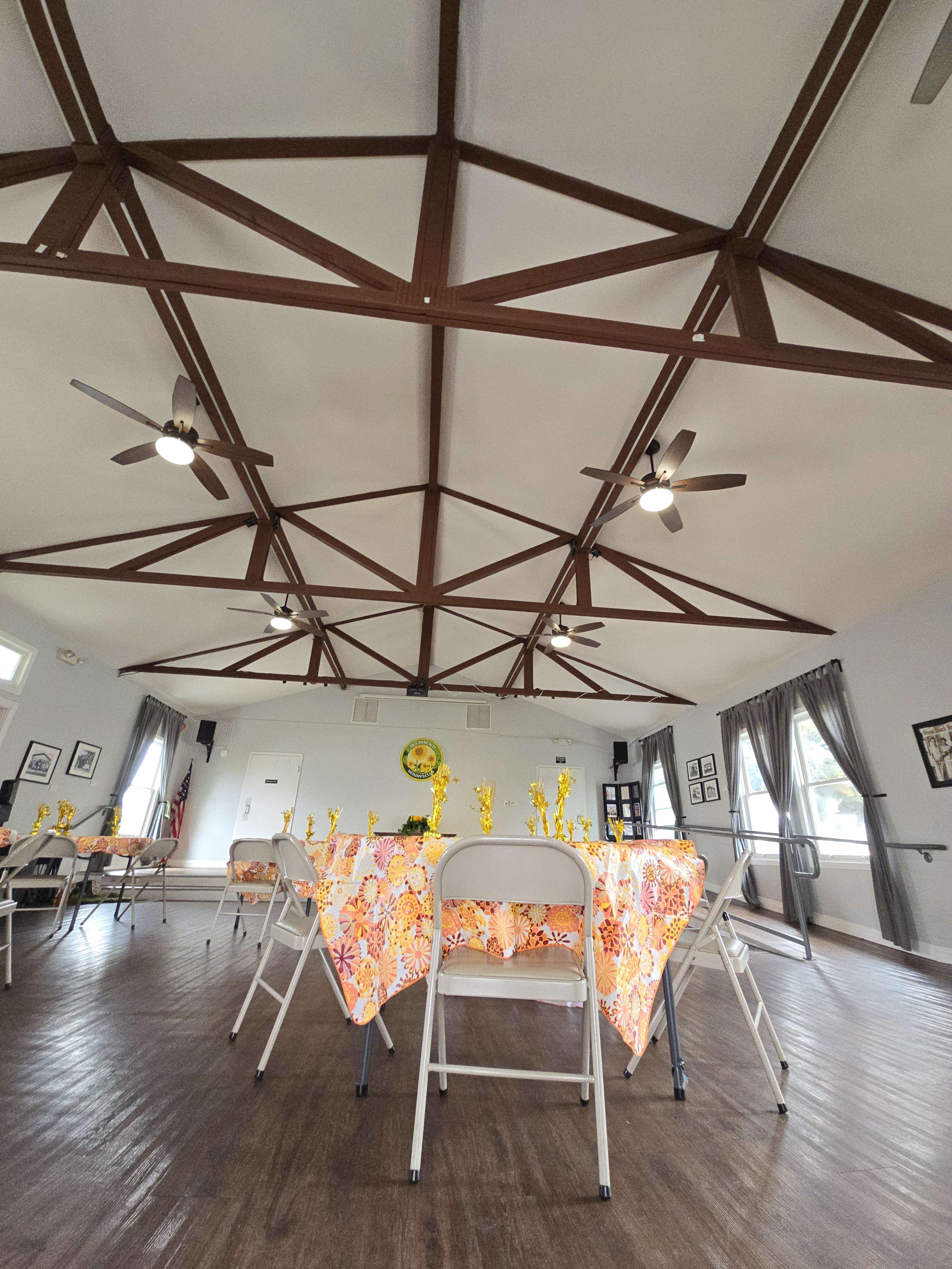 An indoor space with several tables covered in floral tablecloths, surrounded by chairs, and a wooden ceiling with exposed beams.
