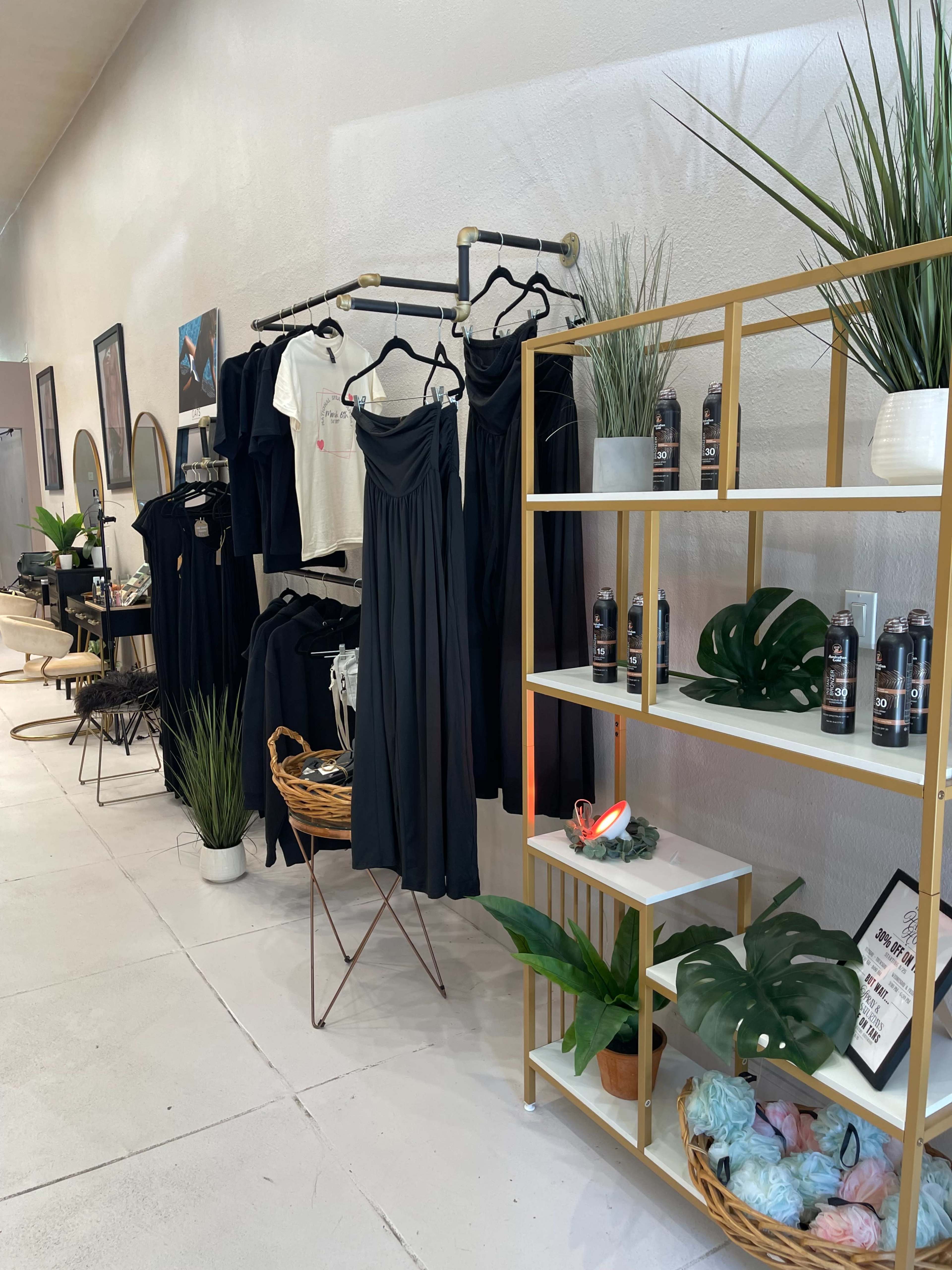 The image shows a boutique interior featuring clothing racks with dresses, shelves displaying beauty products, and potted plants.