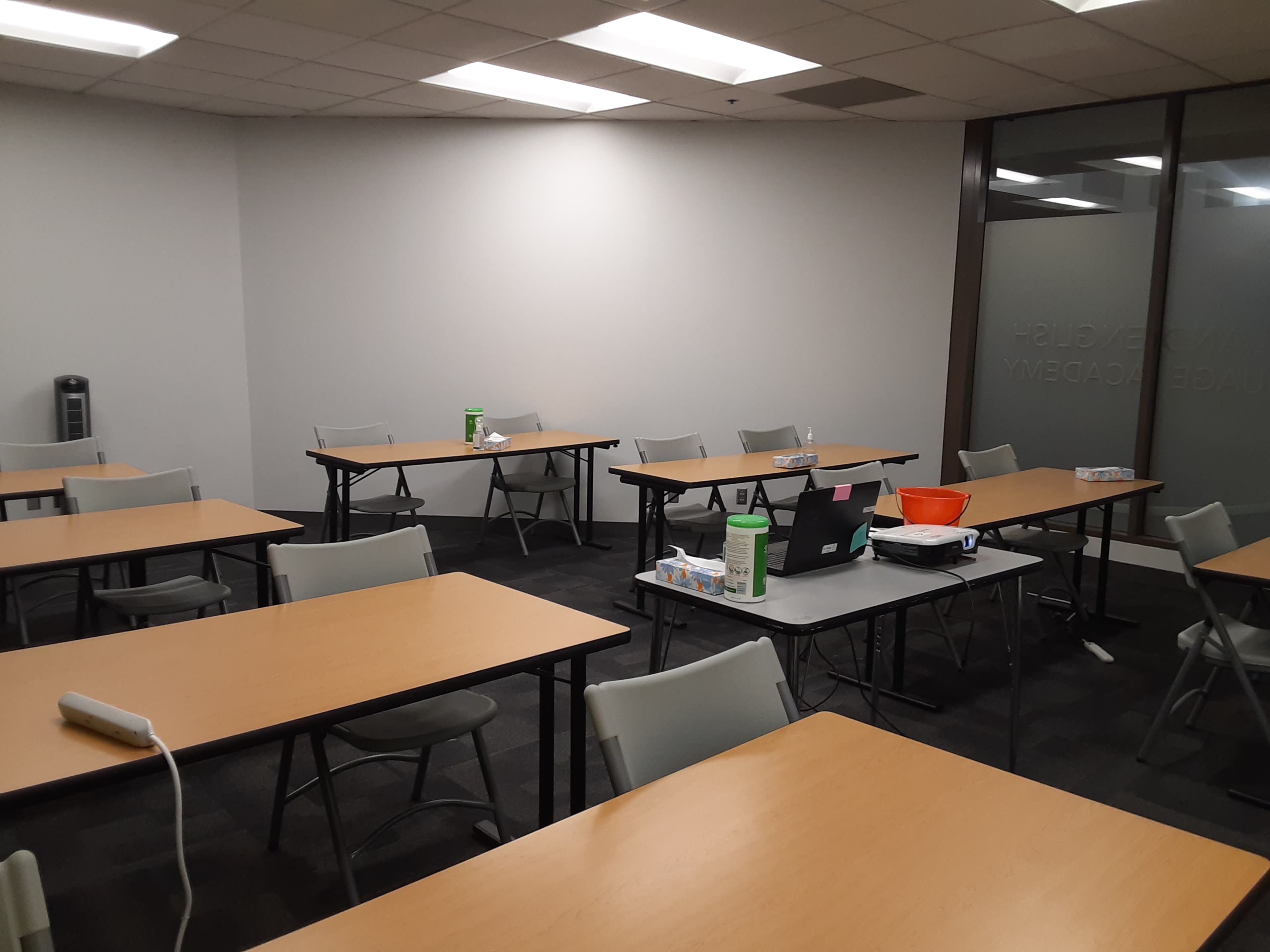 A classroom with several empty tables and chairs arranged in a spacious layout.