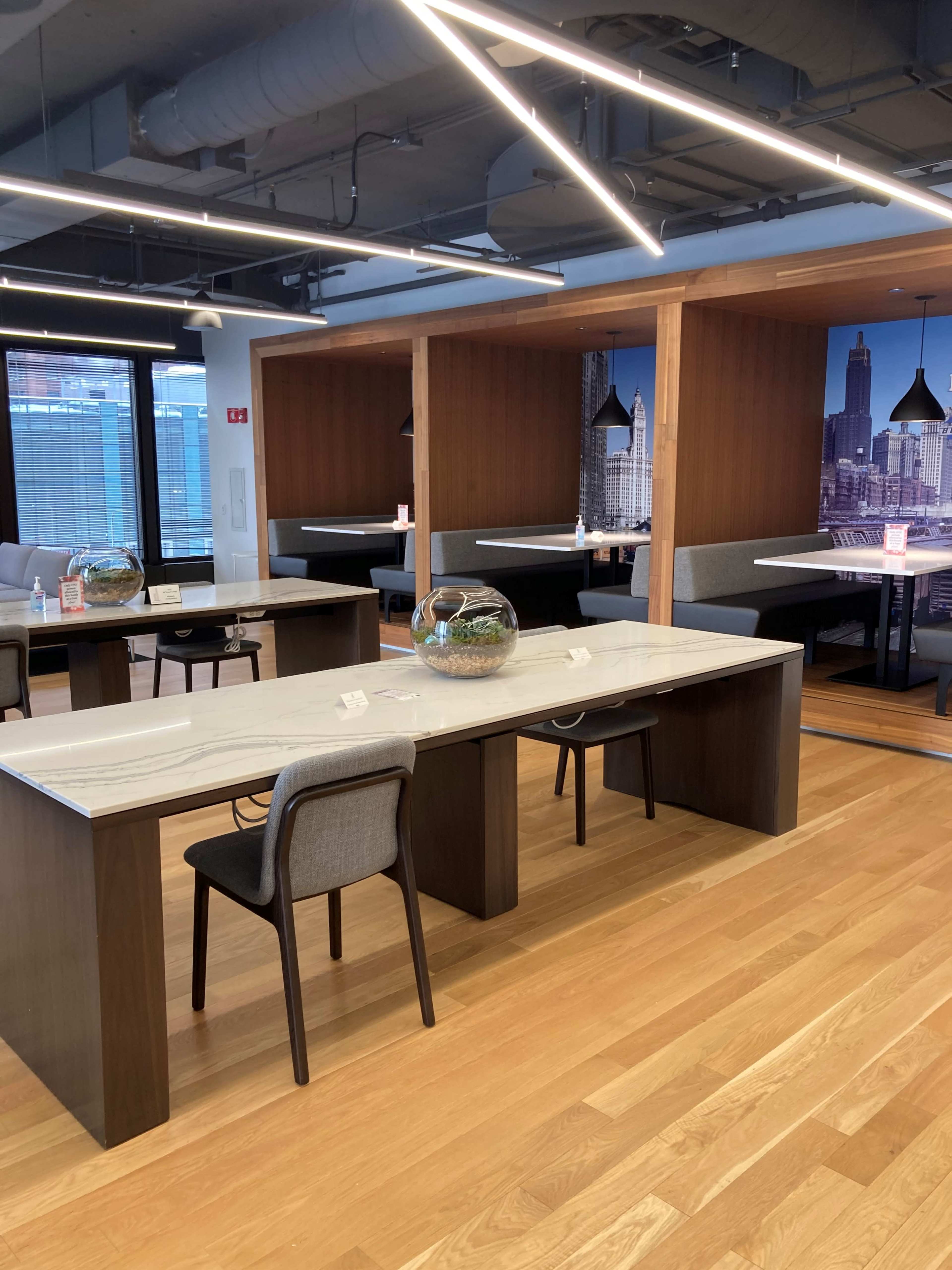 The image shows a modern dining area with sleek wooden tables, gray chairs, and private booths decorated with a city skyline mural.