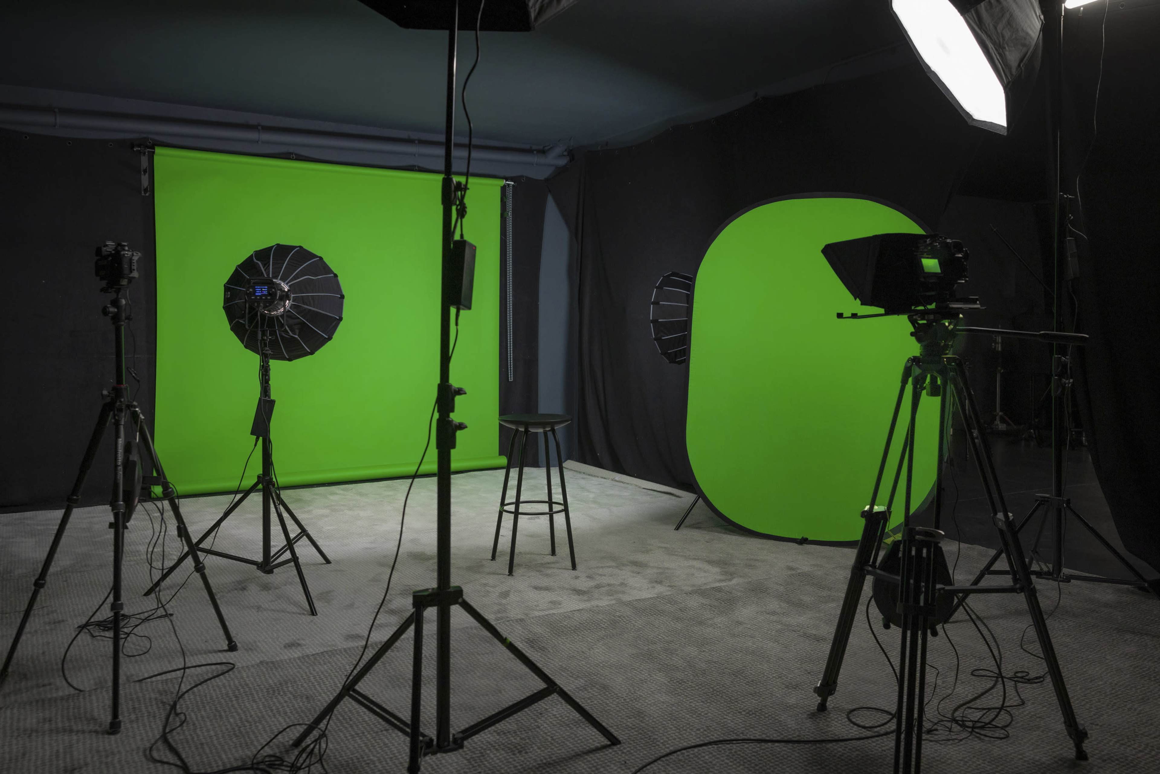 A photography studio features green screens and lighting equipment arranged around a central stool.