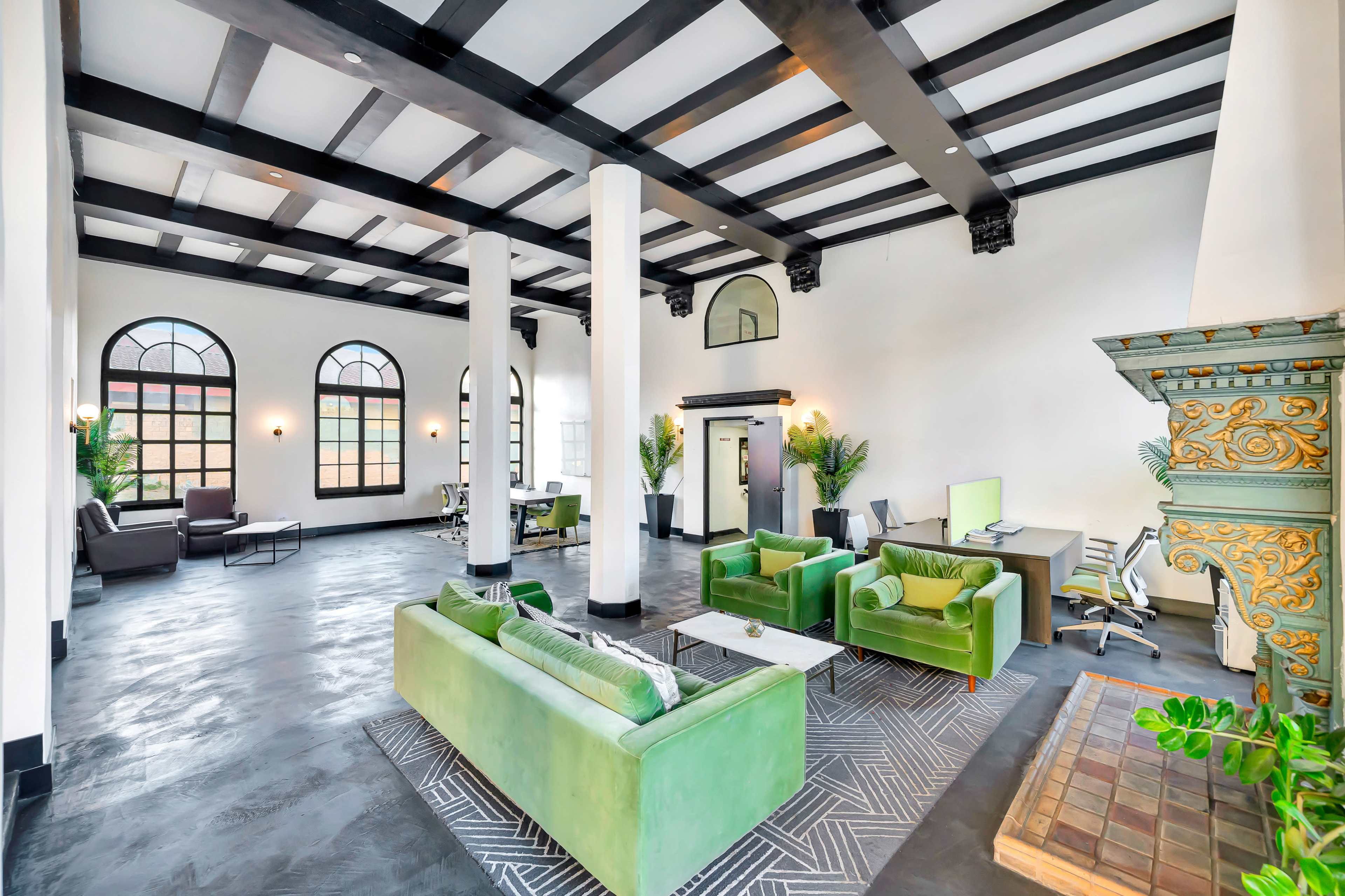 The image shows a spacious interior with high ceilings, featuring green sofas, large windows, and an ornate fireplace.