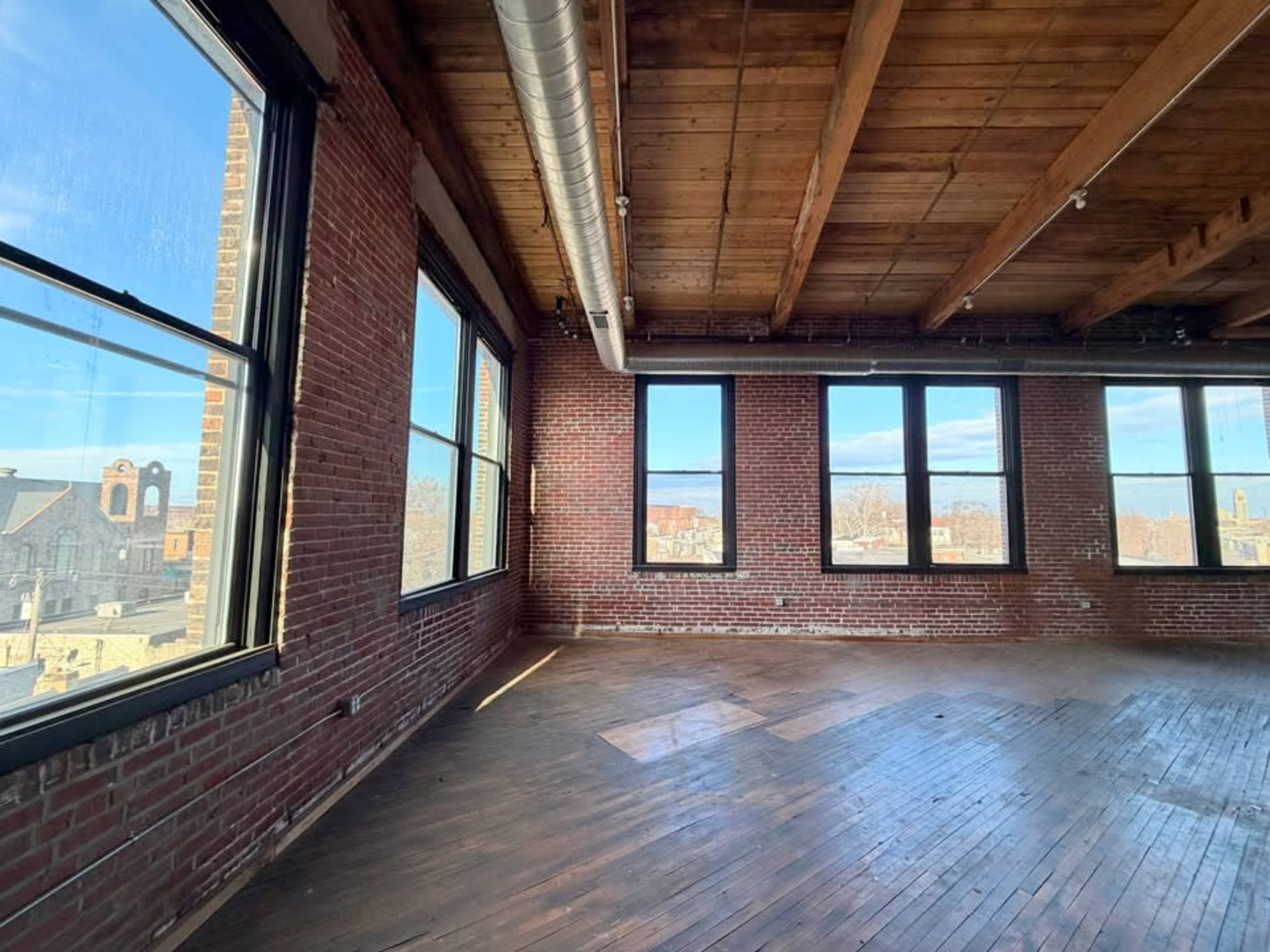 An empty room with wooden floors and large windows showcasing a view of buildings outside.
