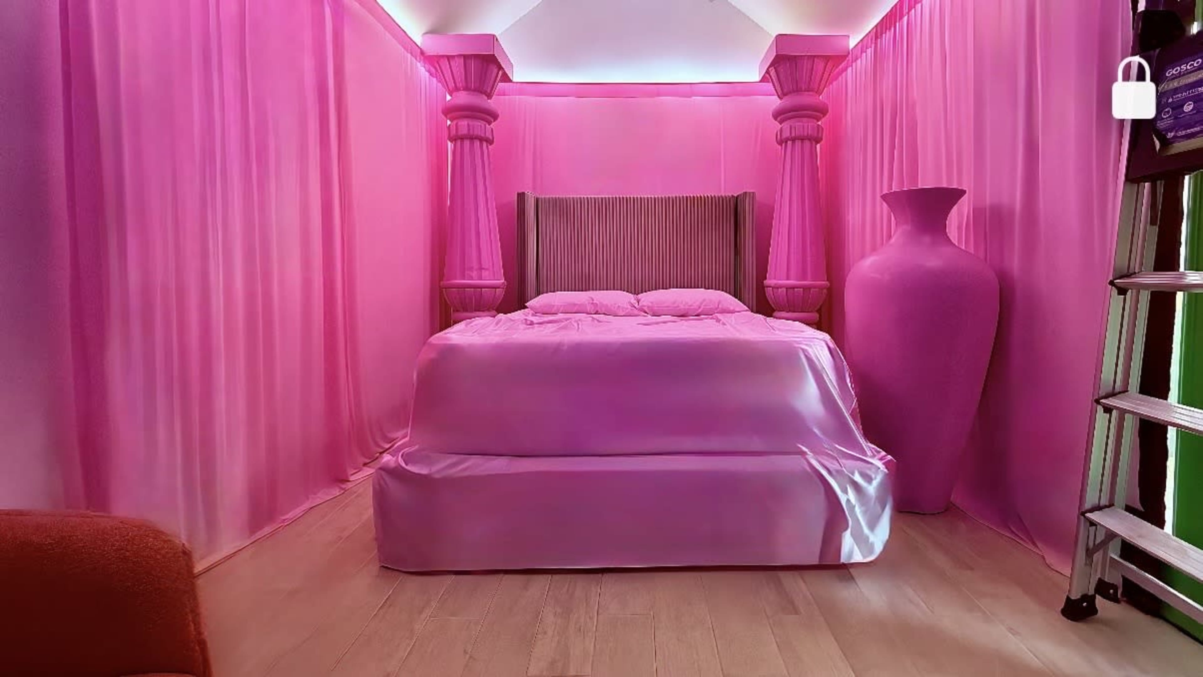 The image shows a bedroom with pink drapery, a pink bedspread, and a large pink vase.