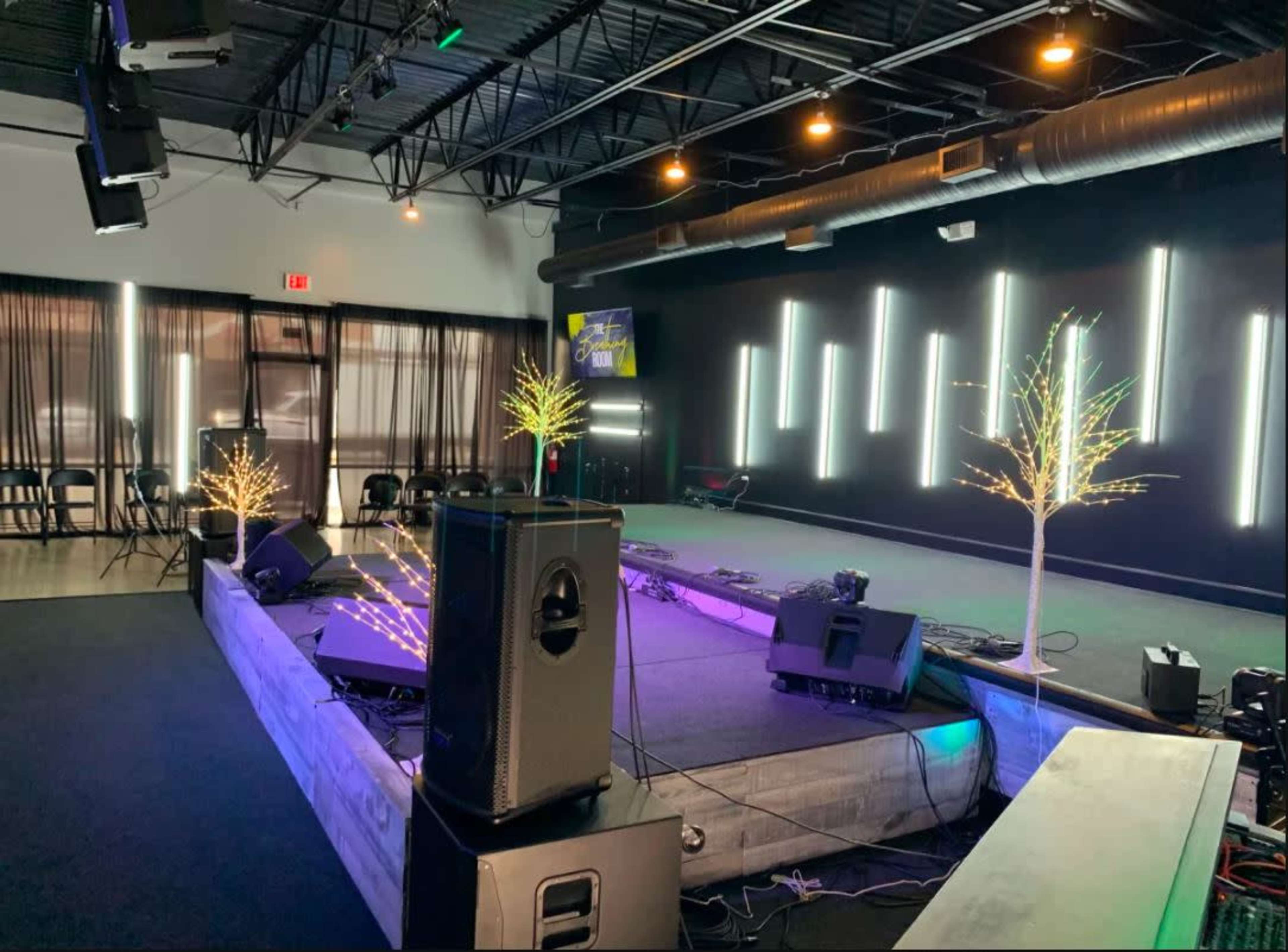 A stage setup in a performance space, featuring speakers, a lighting installation, and illuminated trees.