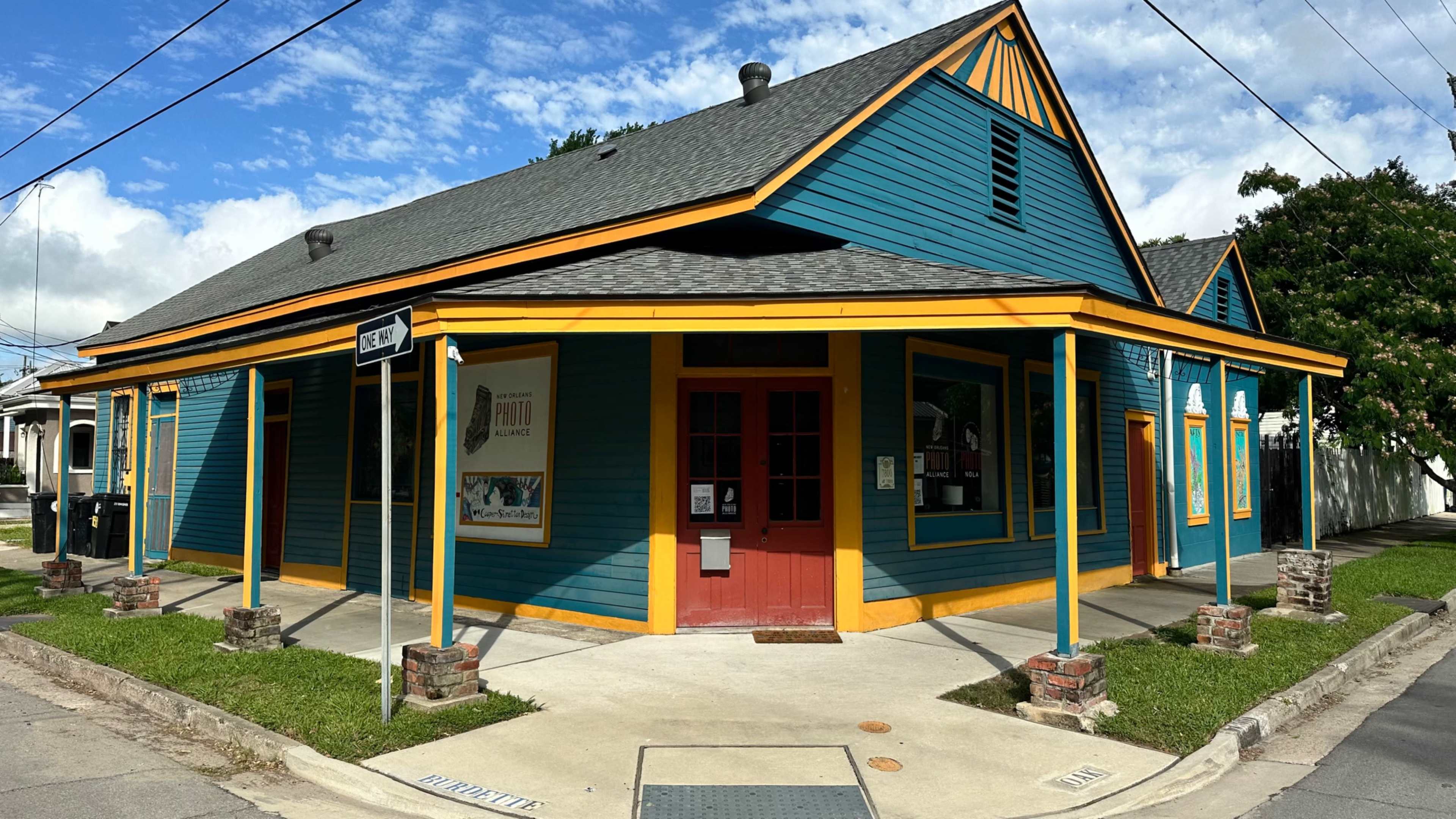 A brightly painted, teal and yellow building with a red door and a wooden sign stands at the corner of a street.