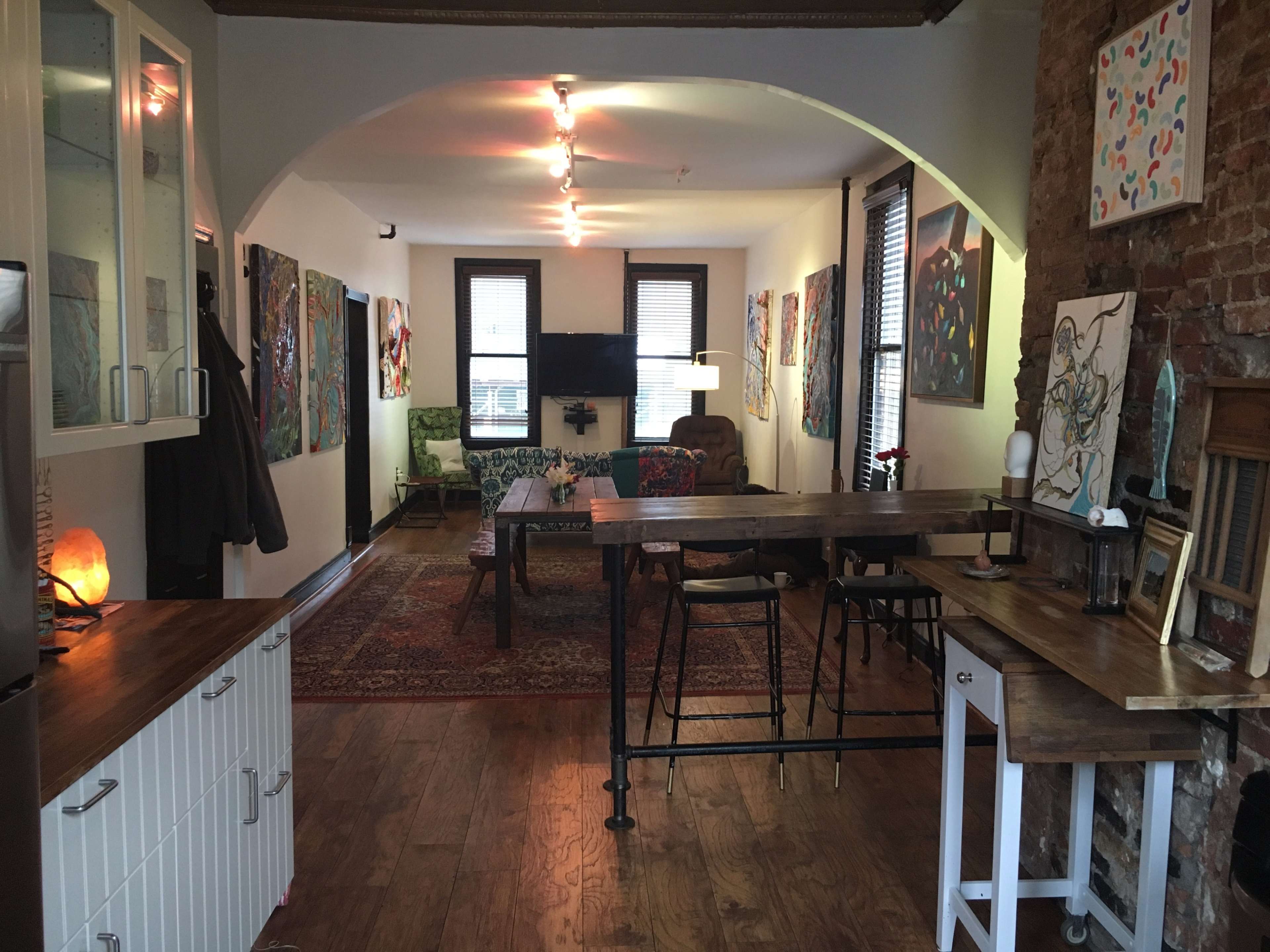 A spacious living area features wooden flooring, art-covered walls, and a mix of seating arrangements, including a couch and dining area.