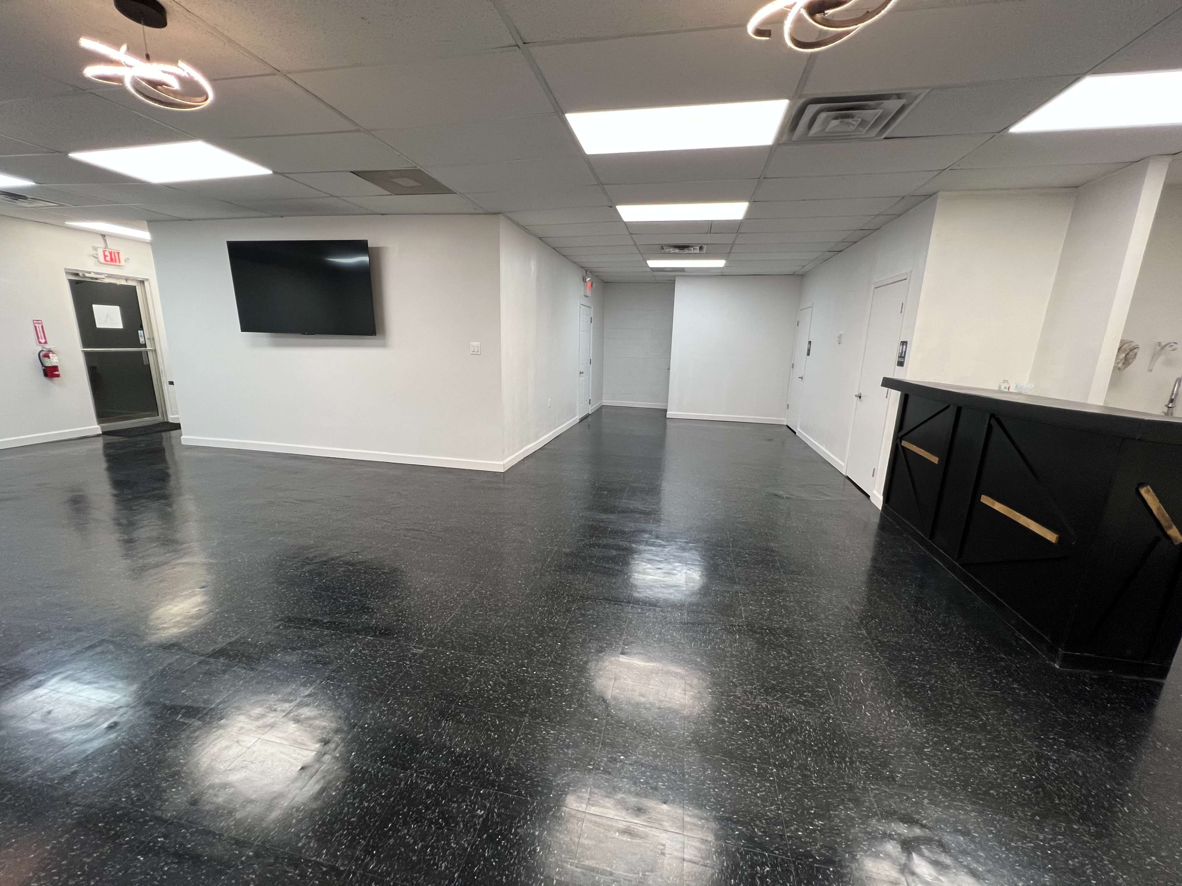 A sparsely furnished room with black tile flooring, bright overhead lights, and a dark countertop against one wall.