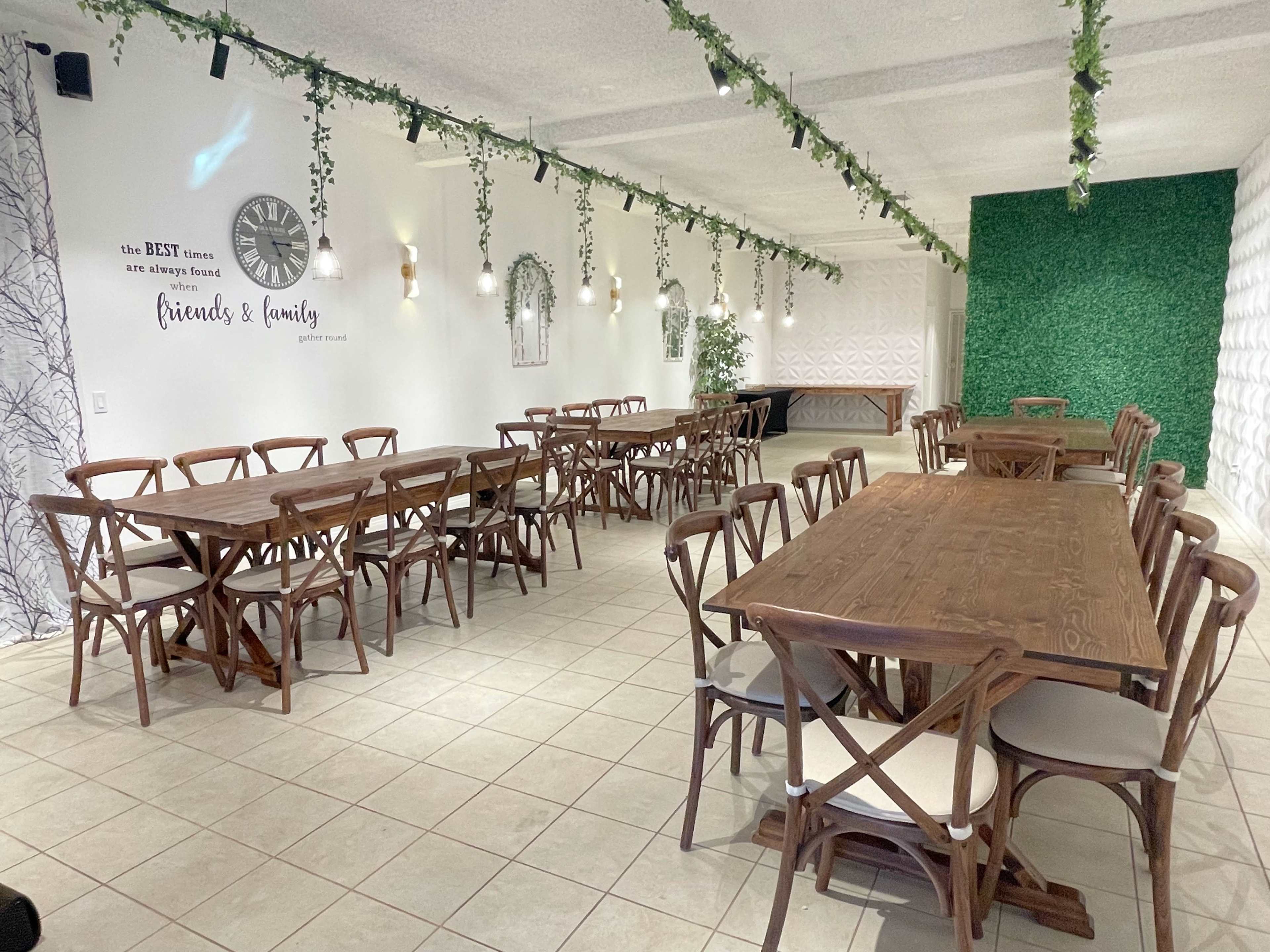A spacious dining area with wooden tables arranged in rows, decorated with greenery along the walls and soft lighting.
