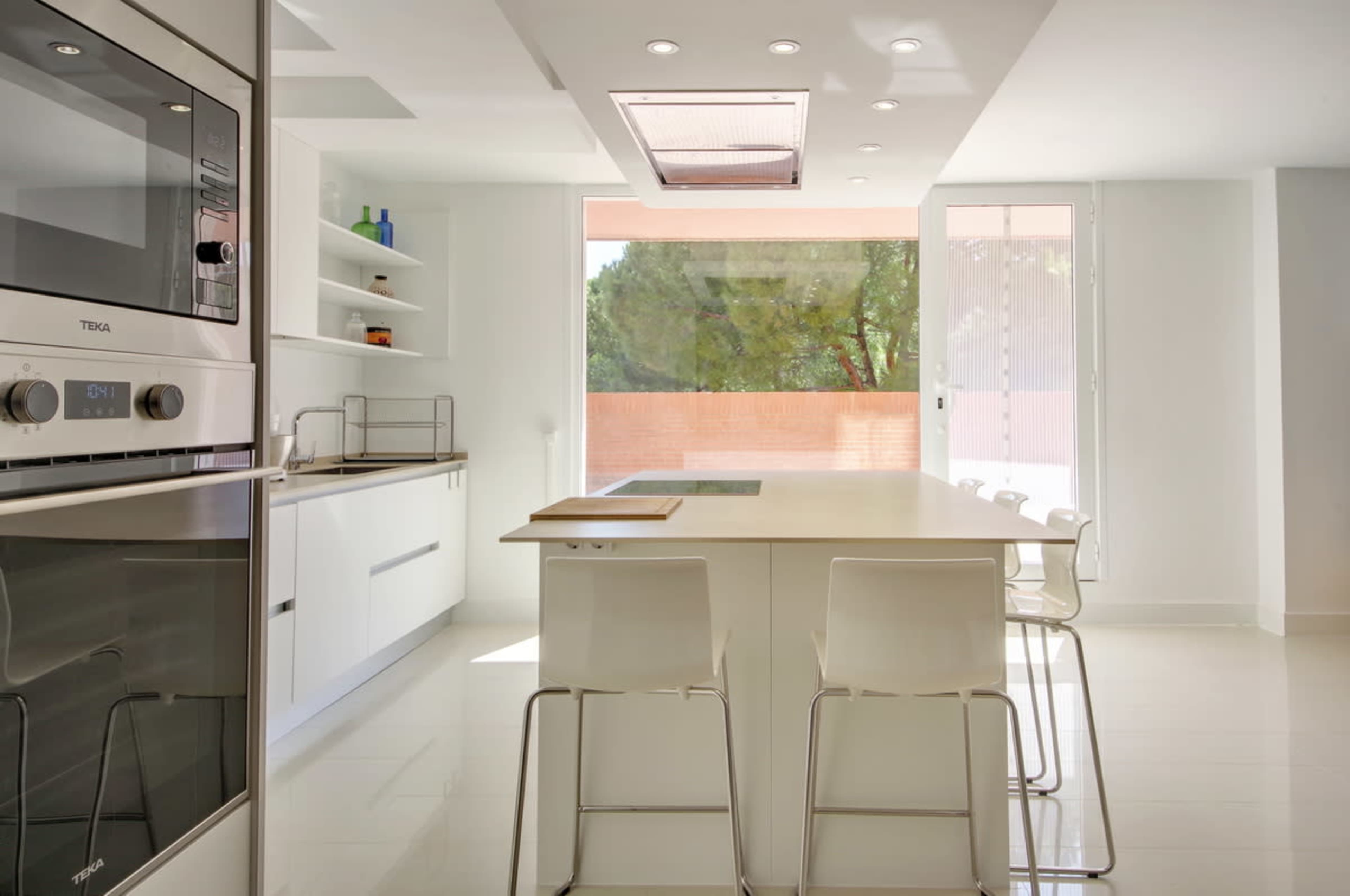 A modern kitchen features white cabinetry, a large central island with seating, and a view of an outdoor space through sliding glass doors.
