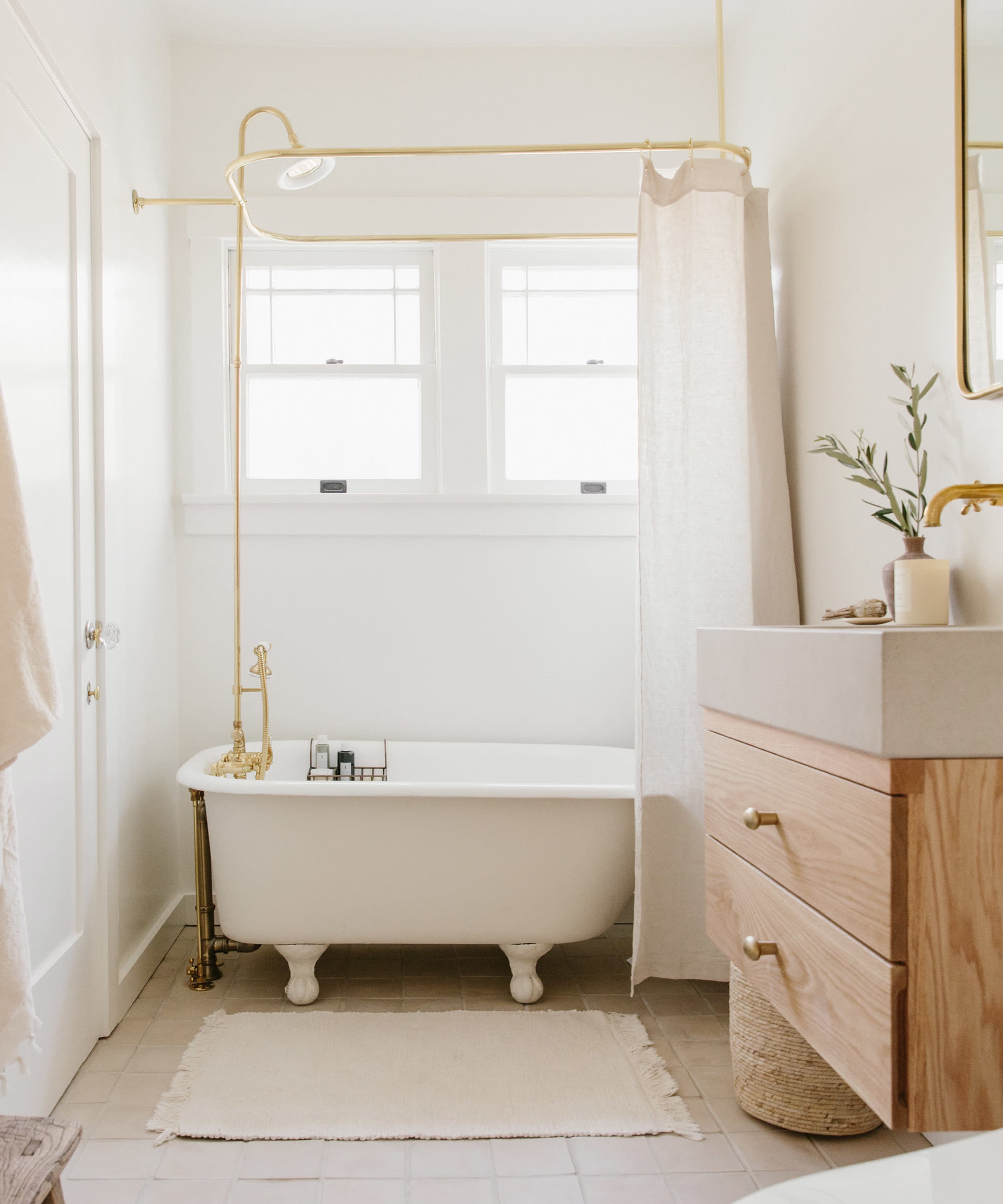 A bright bathroom featuring a clawfoot bathtub, a modern sink with wooden cabinetry, and natural light coming through two windows.