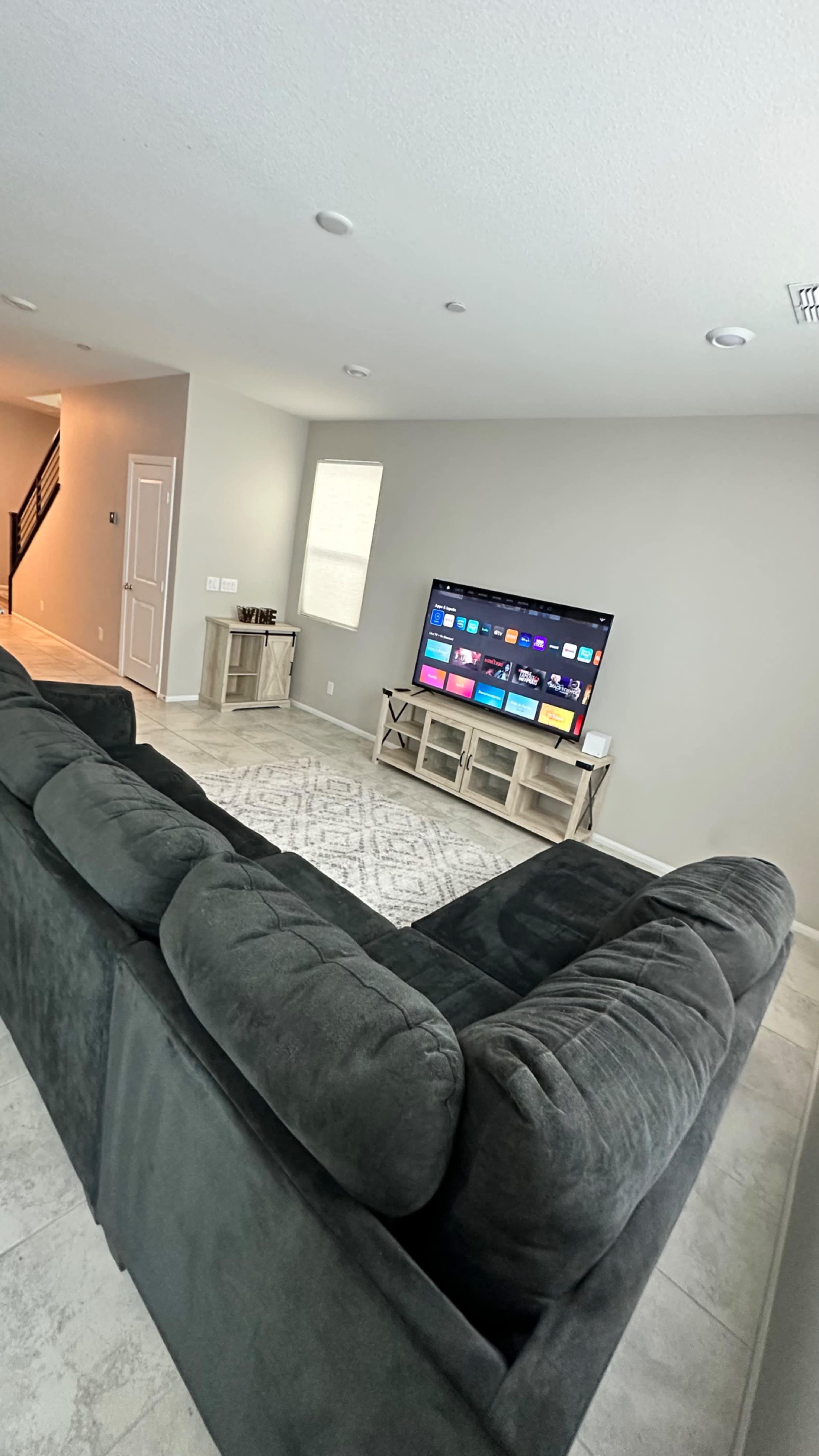 A sectional sofa faces a television mounted on a light-colored wall in a sparsely furnished living room.