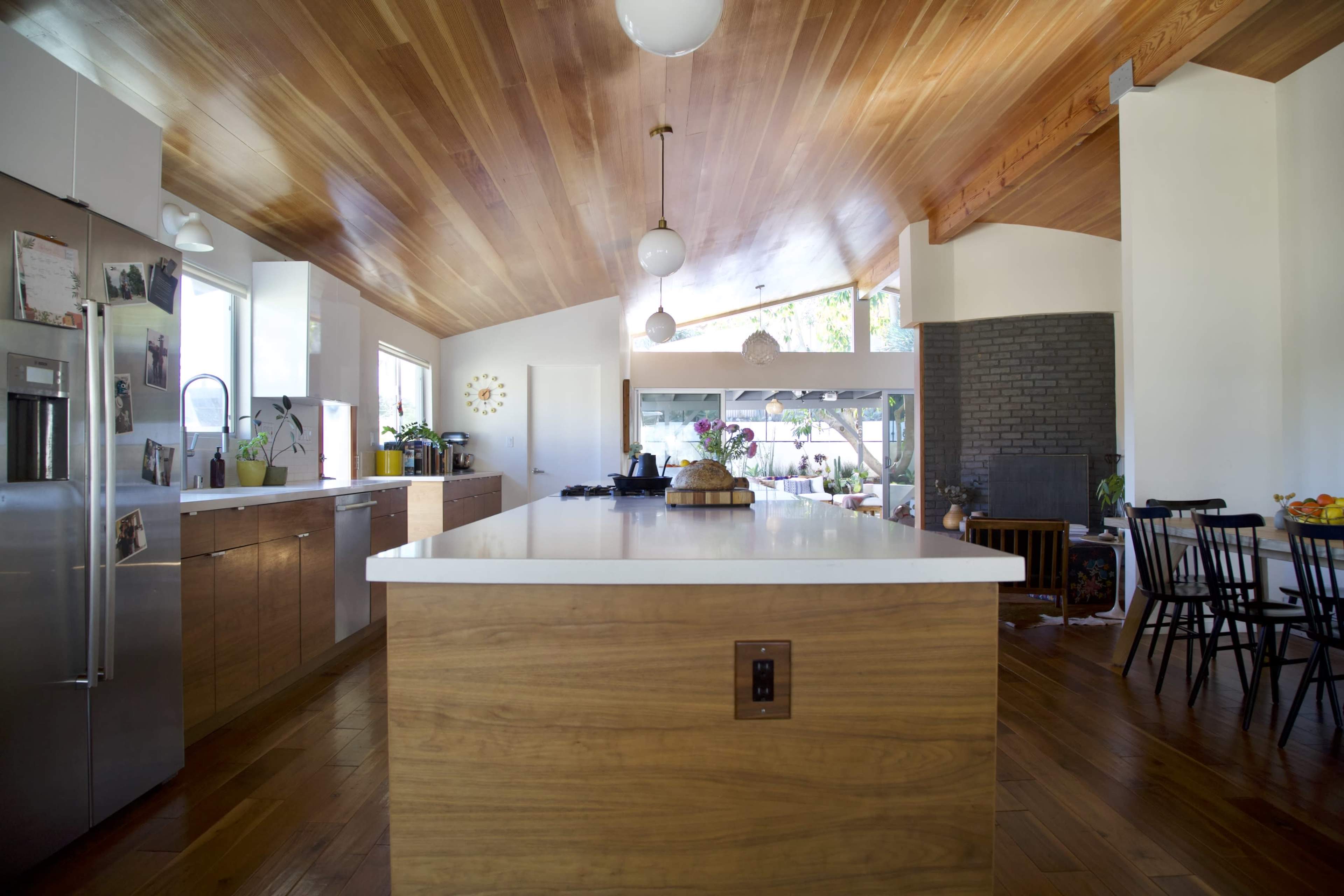 A modern kitchen features a large island with a white countertop, wooden cabinetry, and pendant lighting.