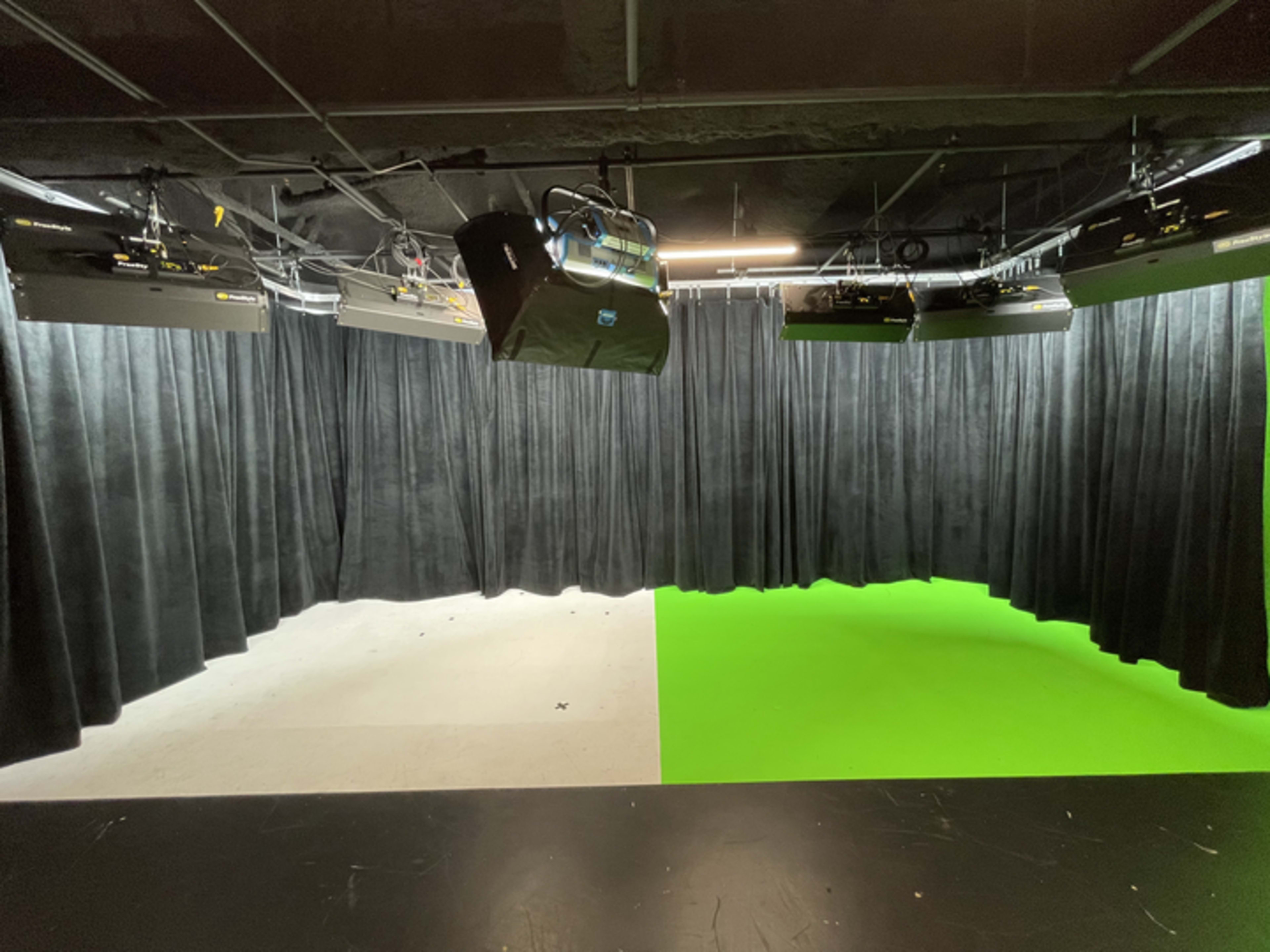 A studio space with a black curtain on one side and a green screen on the other, with overhead lights positioned above.