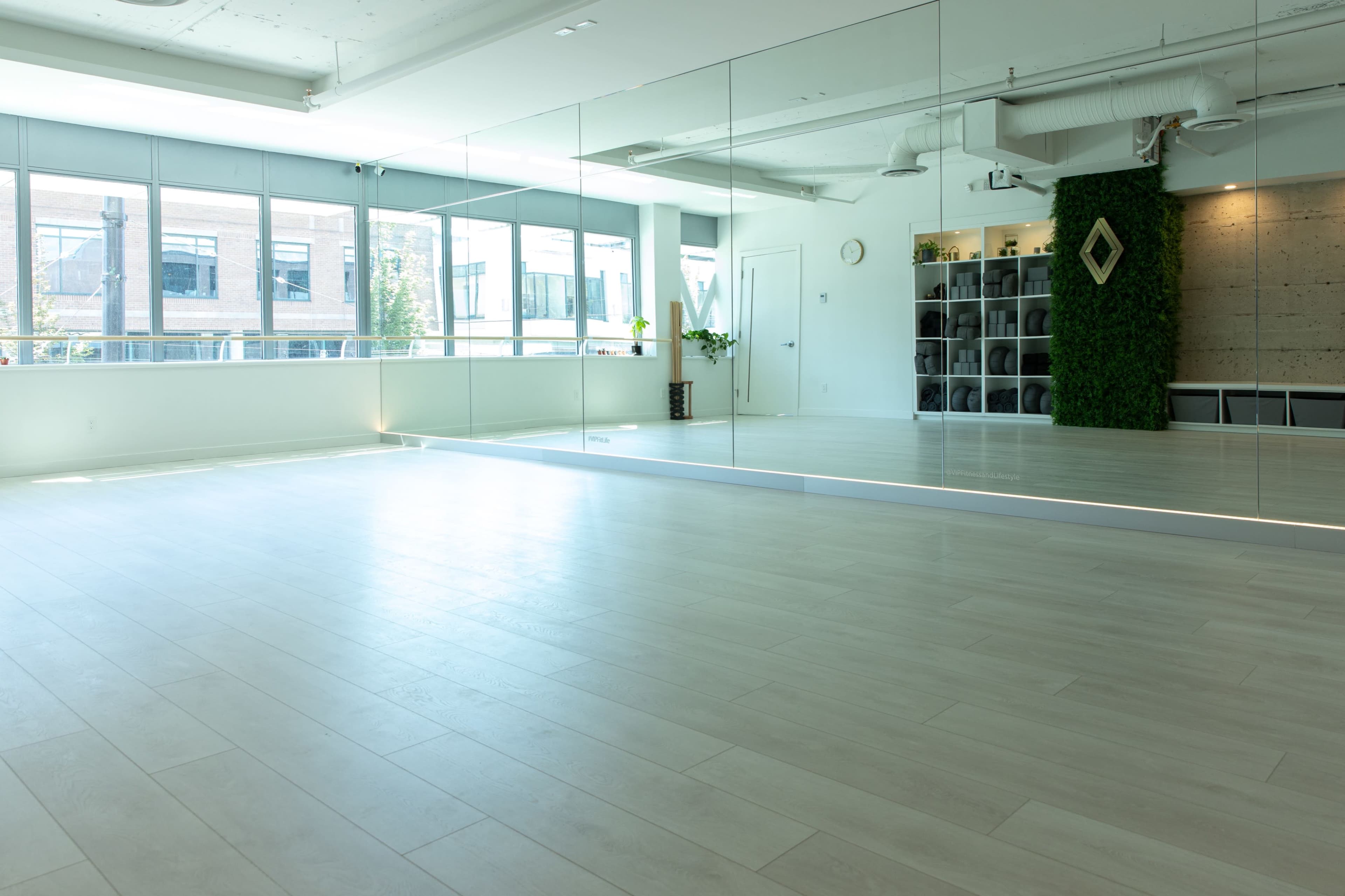 A spacious, well-lit studio with large mirrors, wooden flooring, and a green wall feature, complemented by shelves in the background.