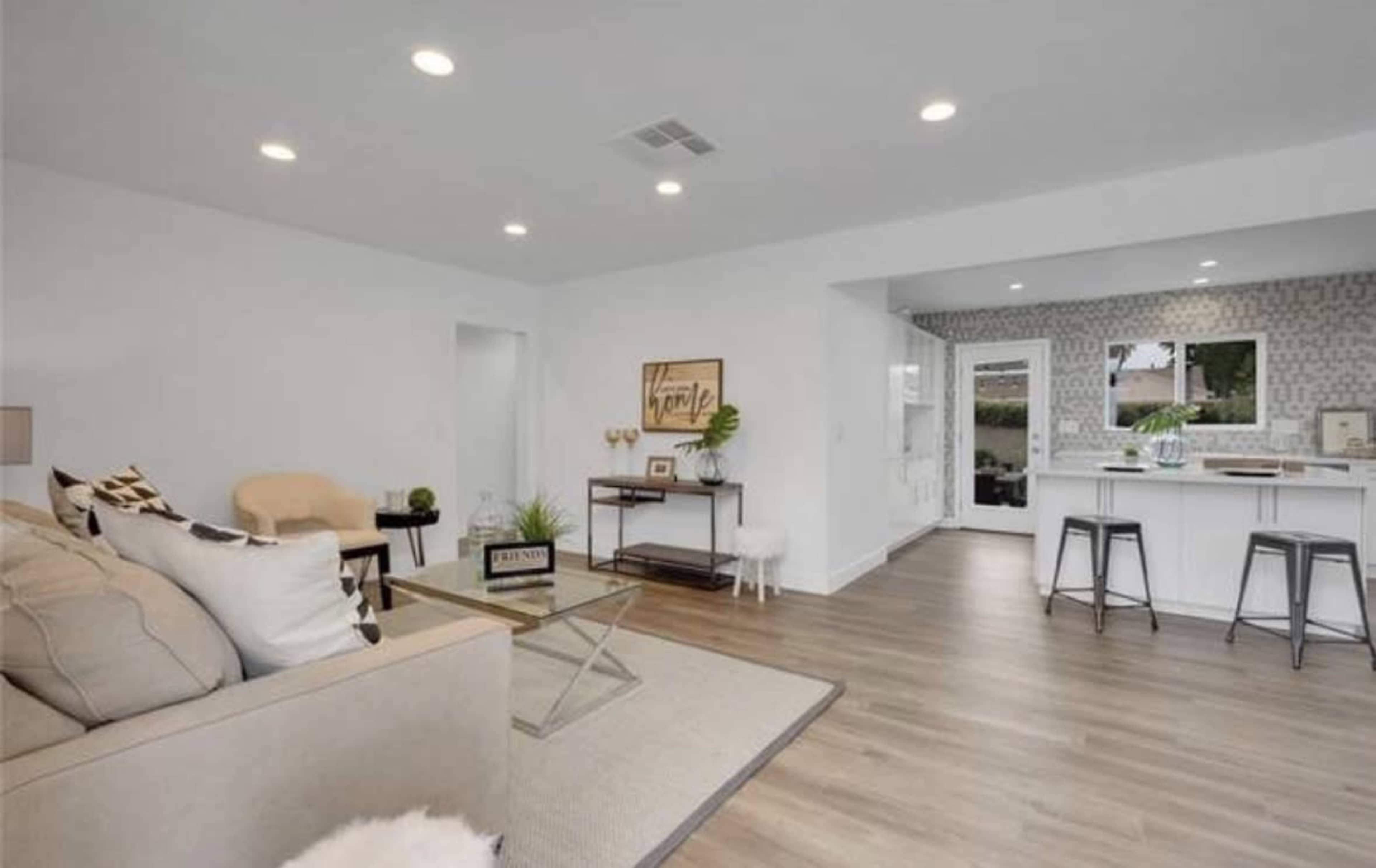 A modern interior living space featuring a light-colored sofa, a glass coffee table, and an open kitchen area with bar stools.