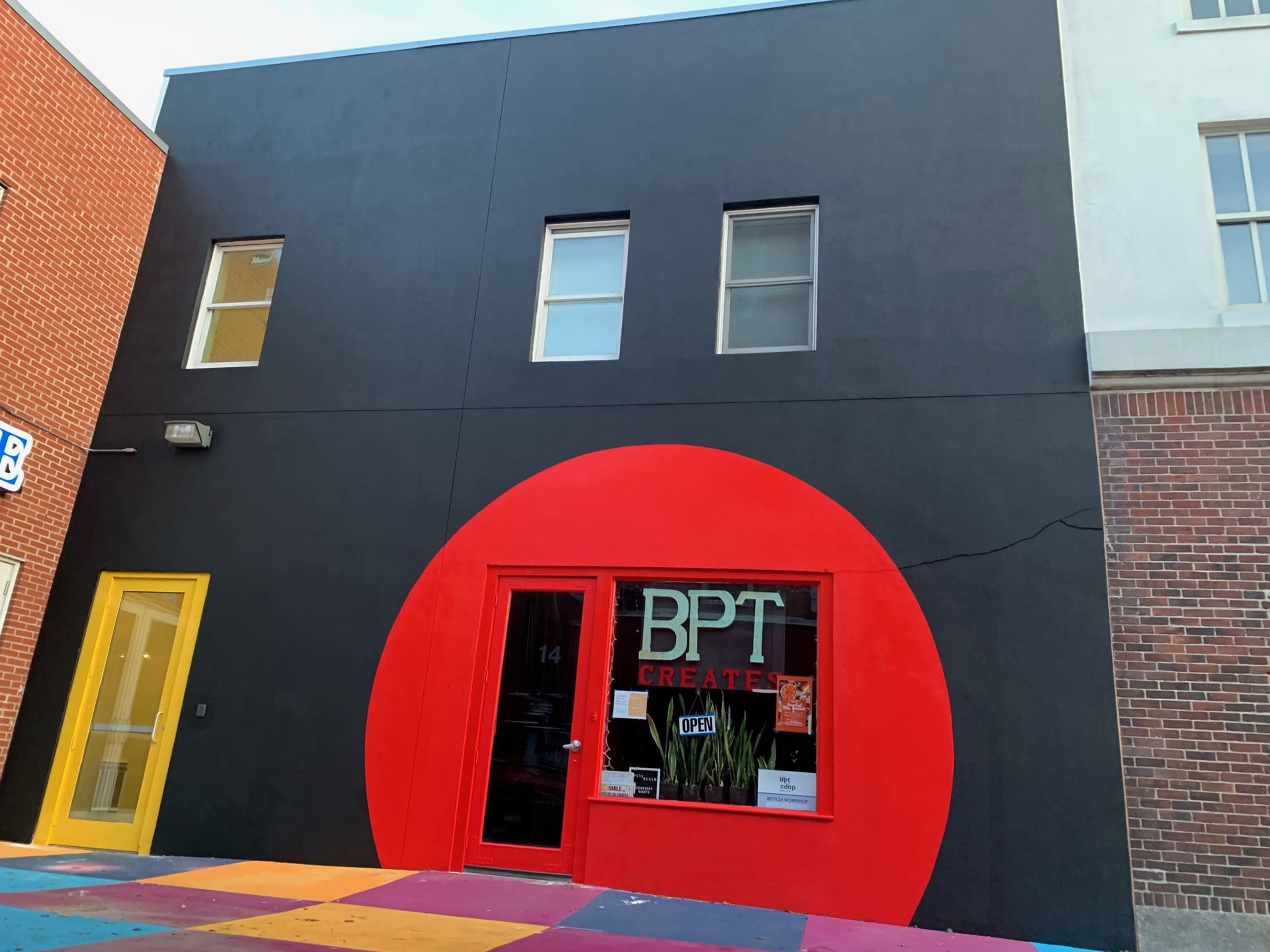 The image shows a building with a black exterior and a large red circular feature around the front window, which displays "BPT CREATIVE" and an "OPEN" sign.