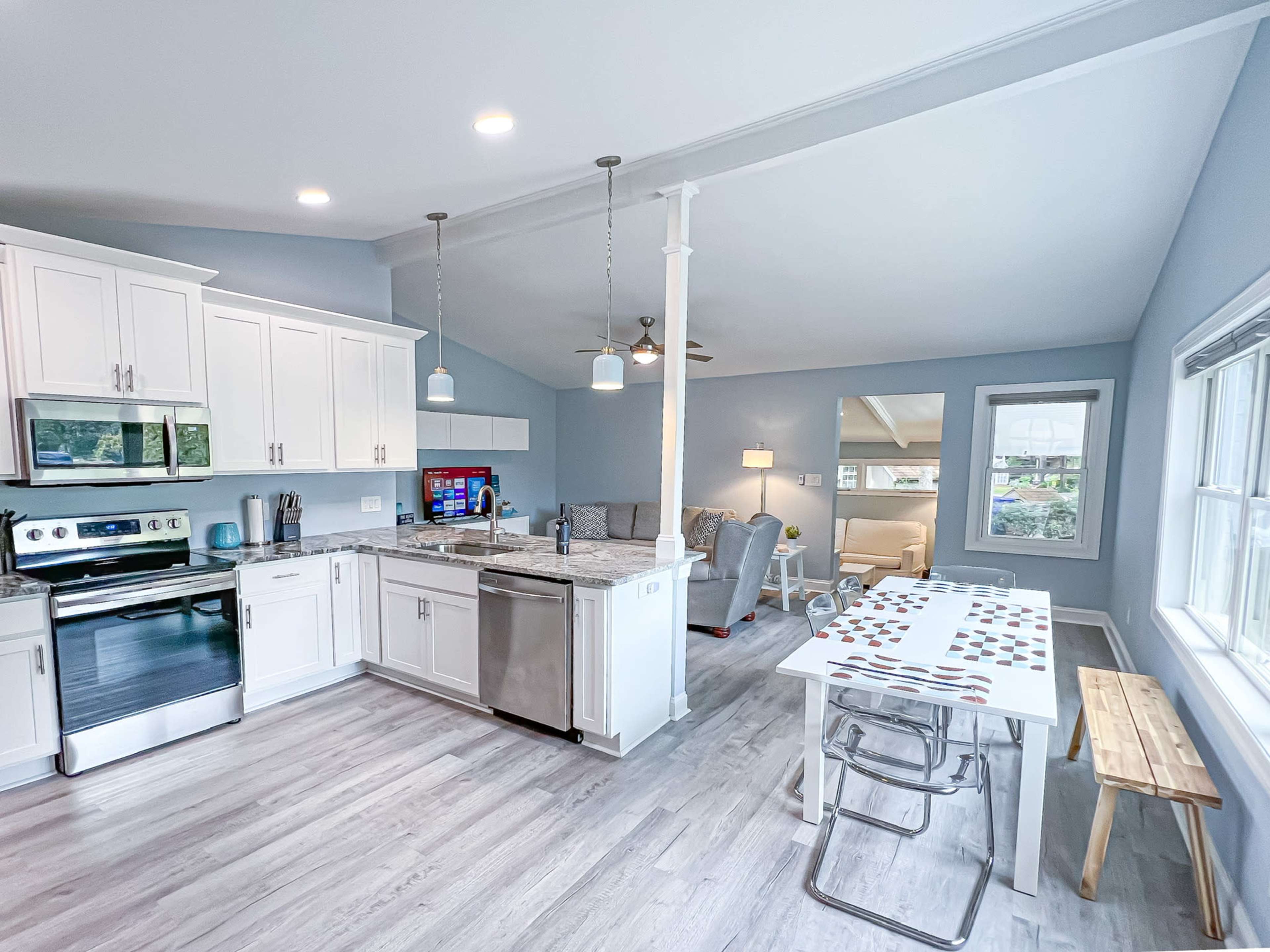 A modern kitchen with white cabinets, stainless steel appliances, and a dining table set for four, adjacent to a cozy living area.