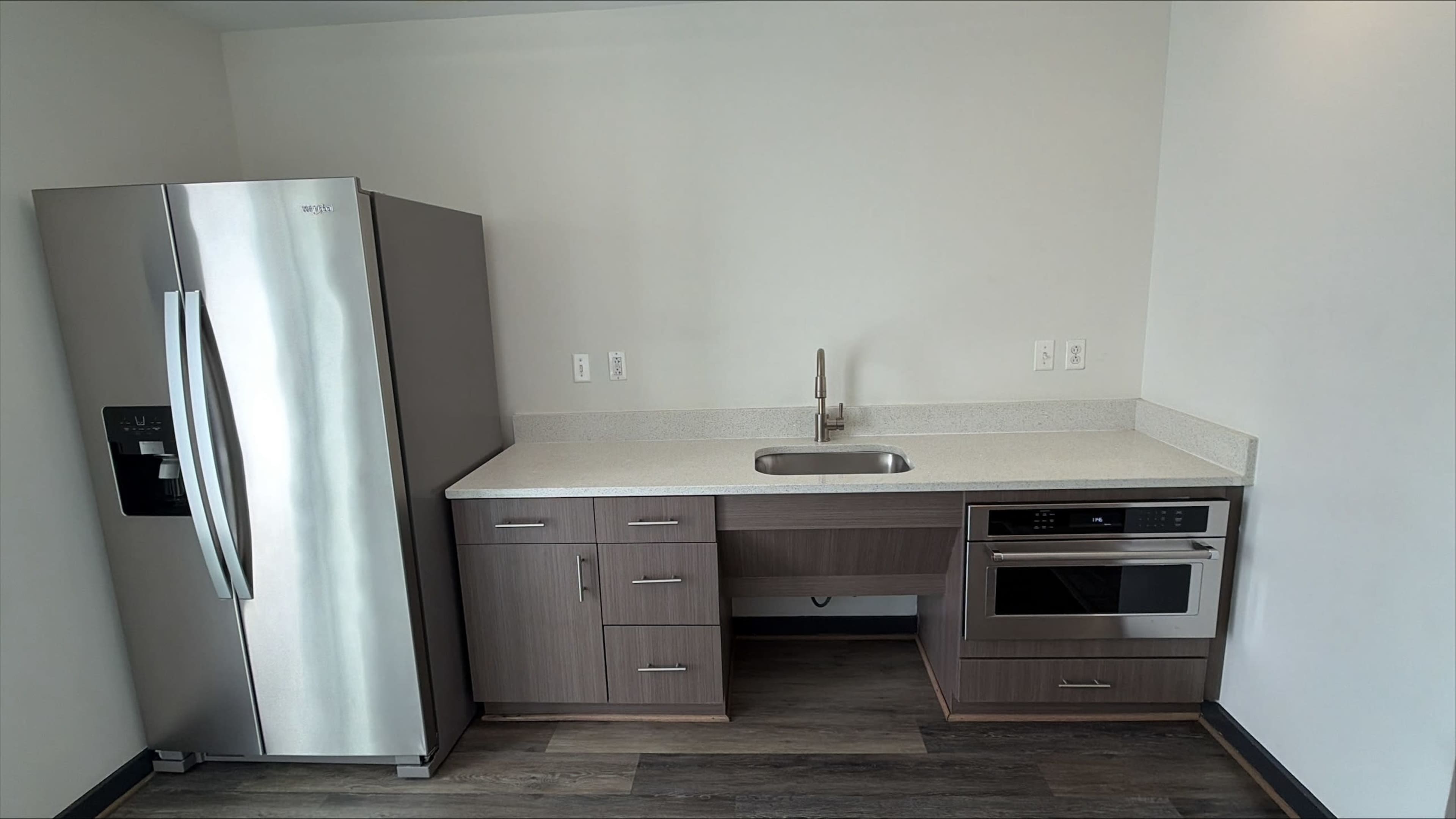 The image shows a modern kitchenette with a stainless steel refrigerator, sink, and built-in microwave.