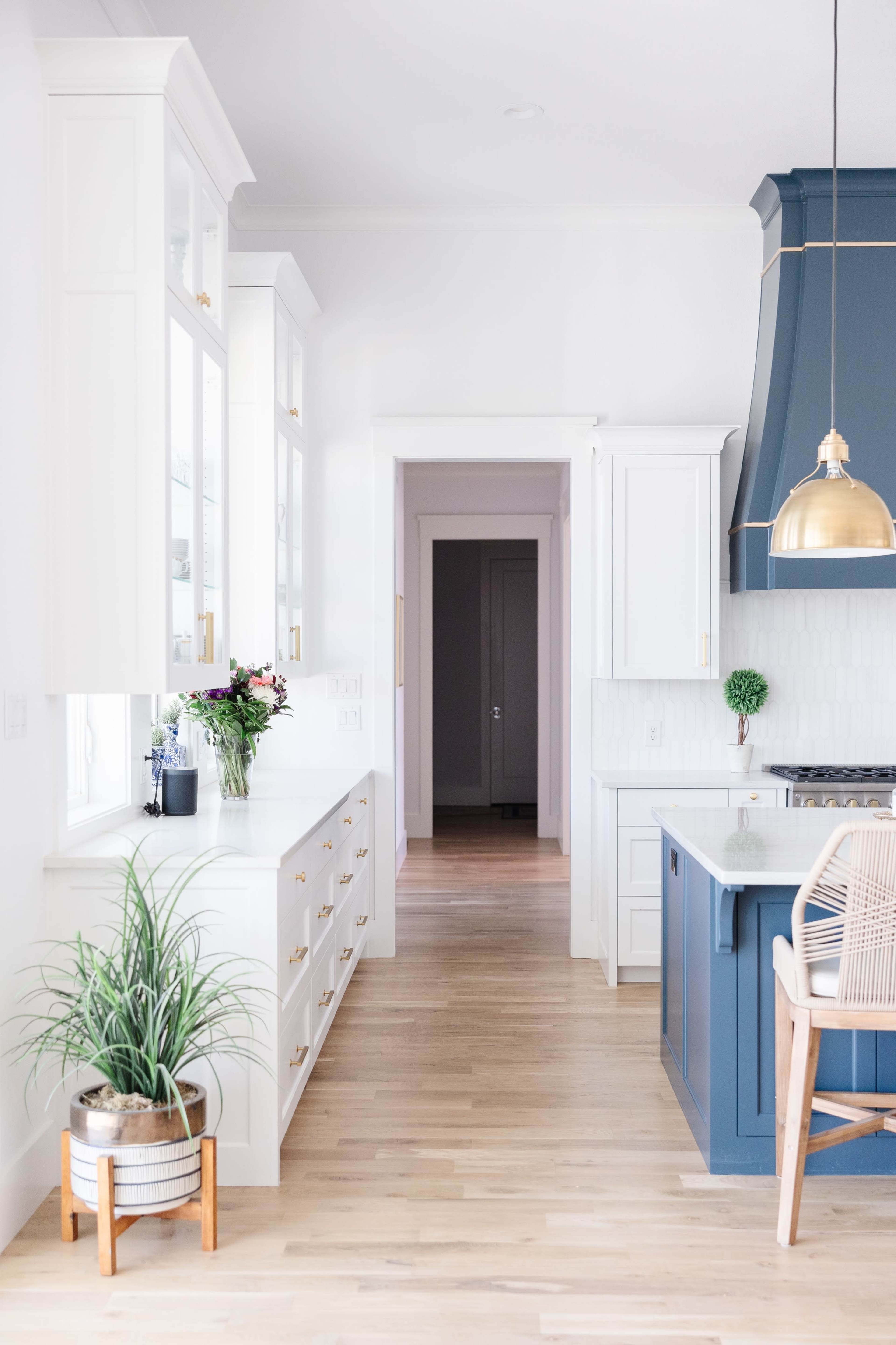 A bright kitchen features a central island with a blue cabinetry, white cabinets along the wall, and a hallway leading to another room.
