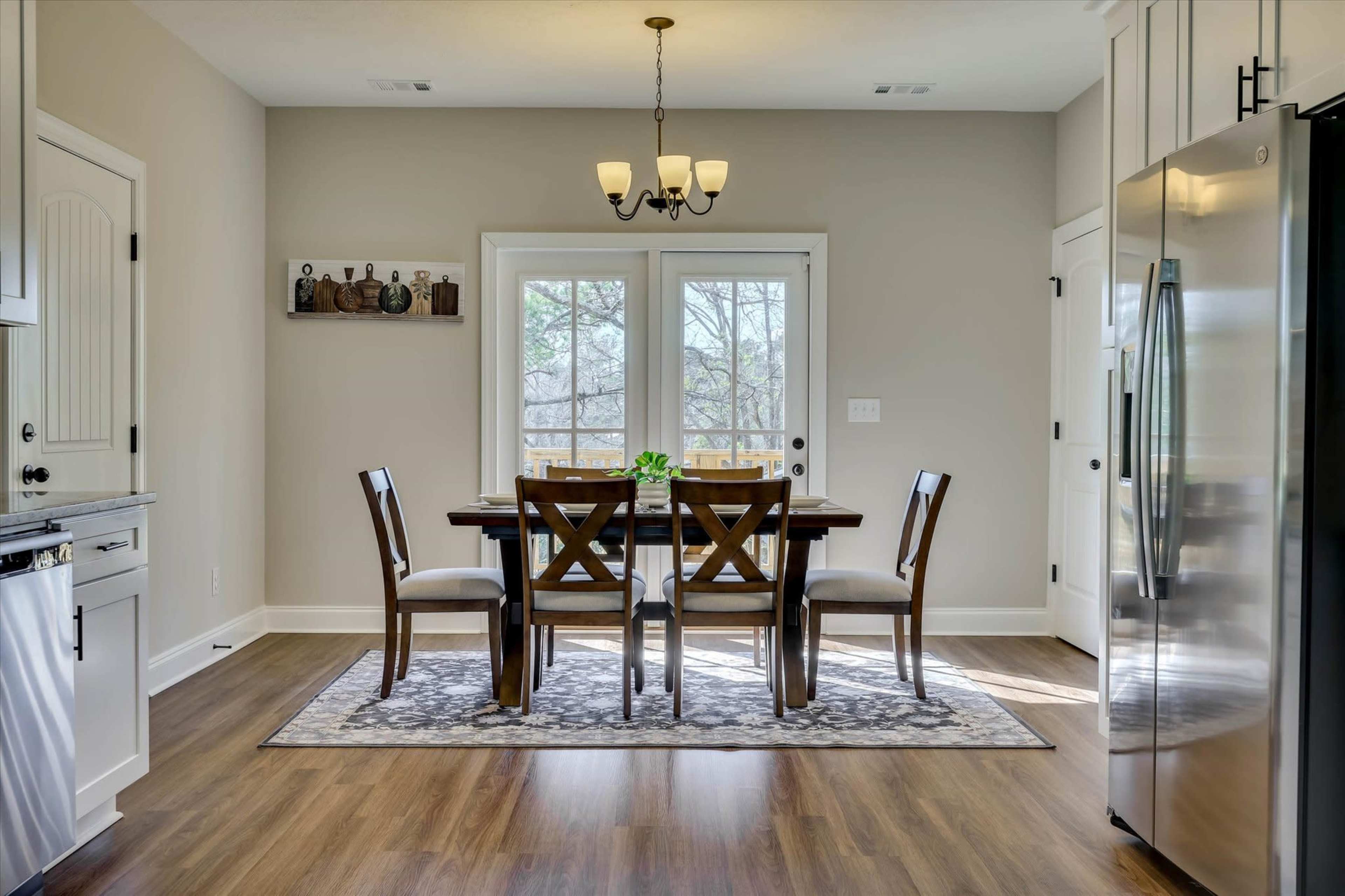 A wooden dining table with chairs is set in a well-lit kitchen, leading to a door with windows that opens to an outdoor view.