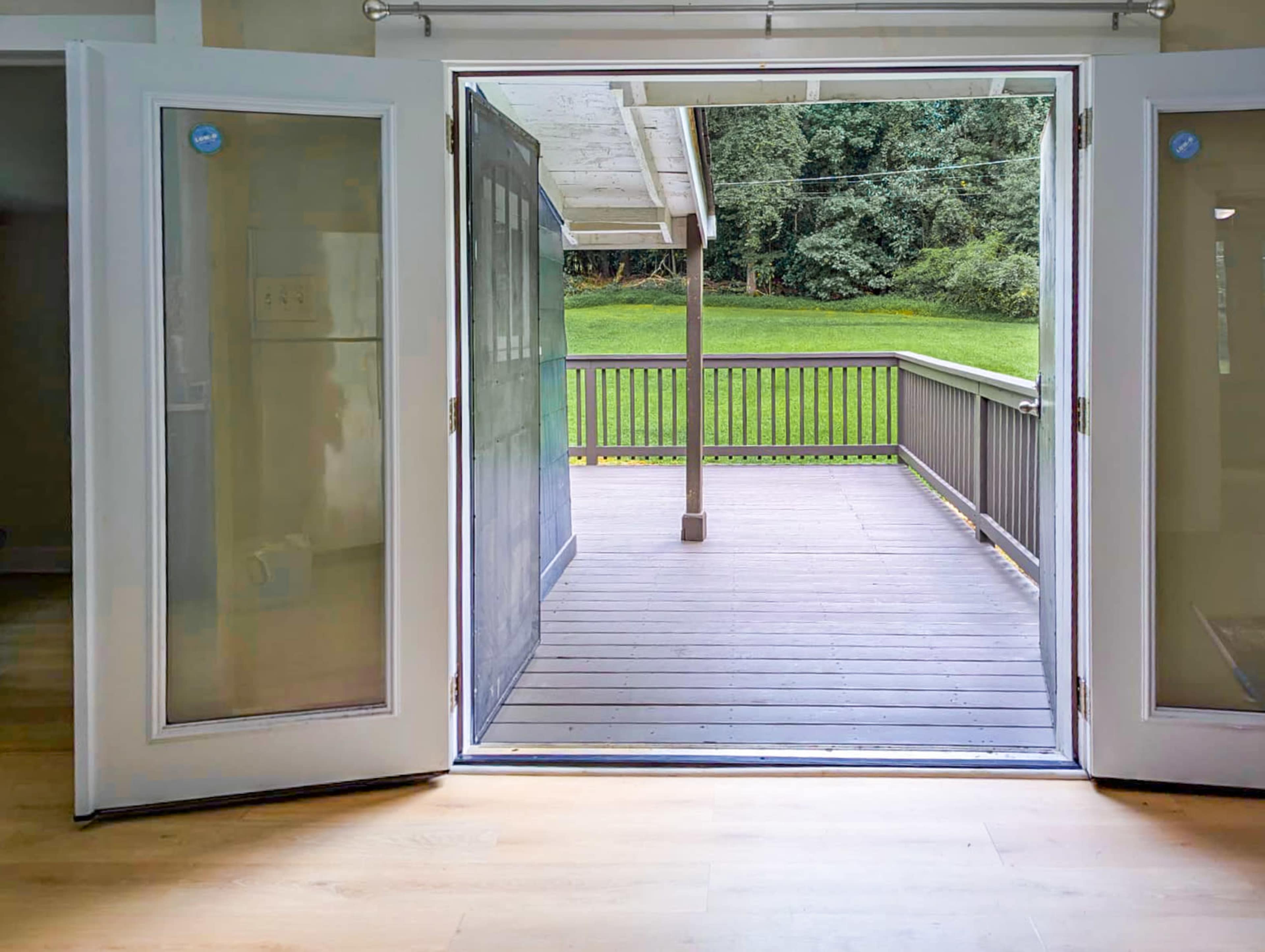 The image shows a pair of open double doors leading to a wooden deck overlooking a green lawn.
