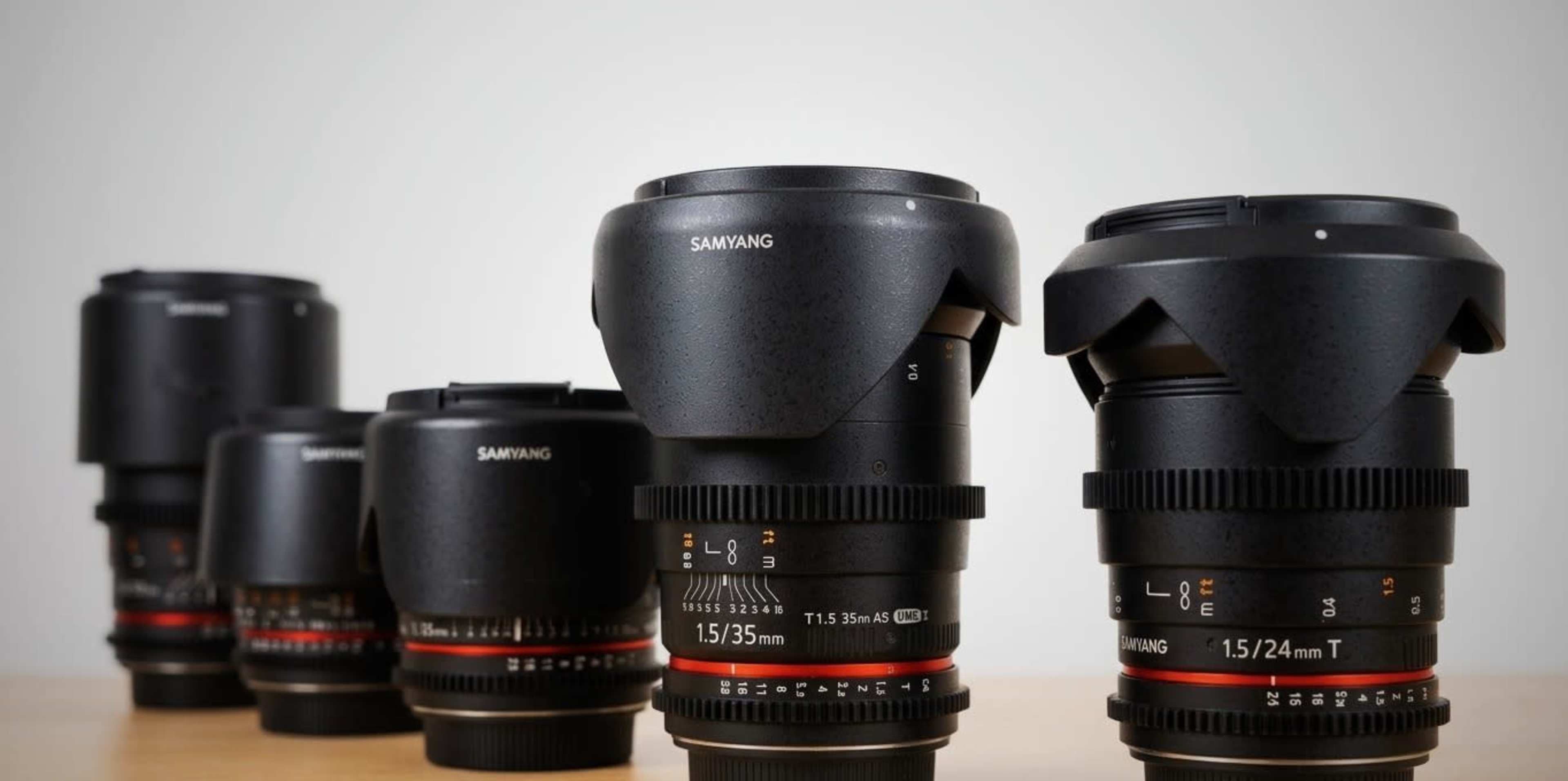 A row of five Samyang camera lenses of varying sizes and specifications is displayed on a wooden surface.