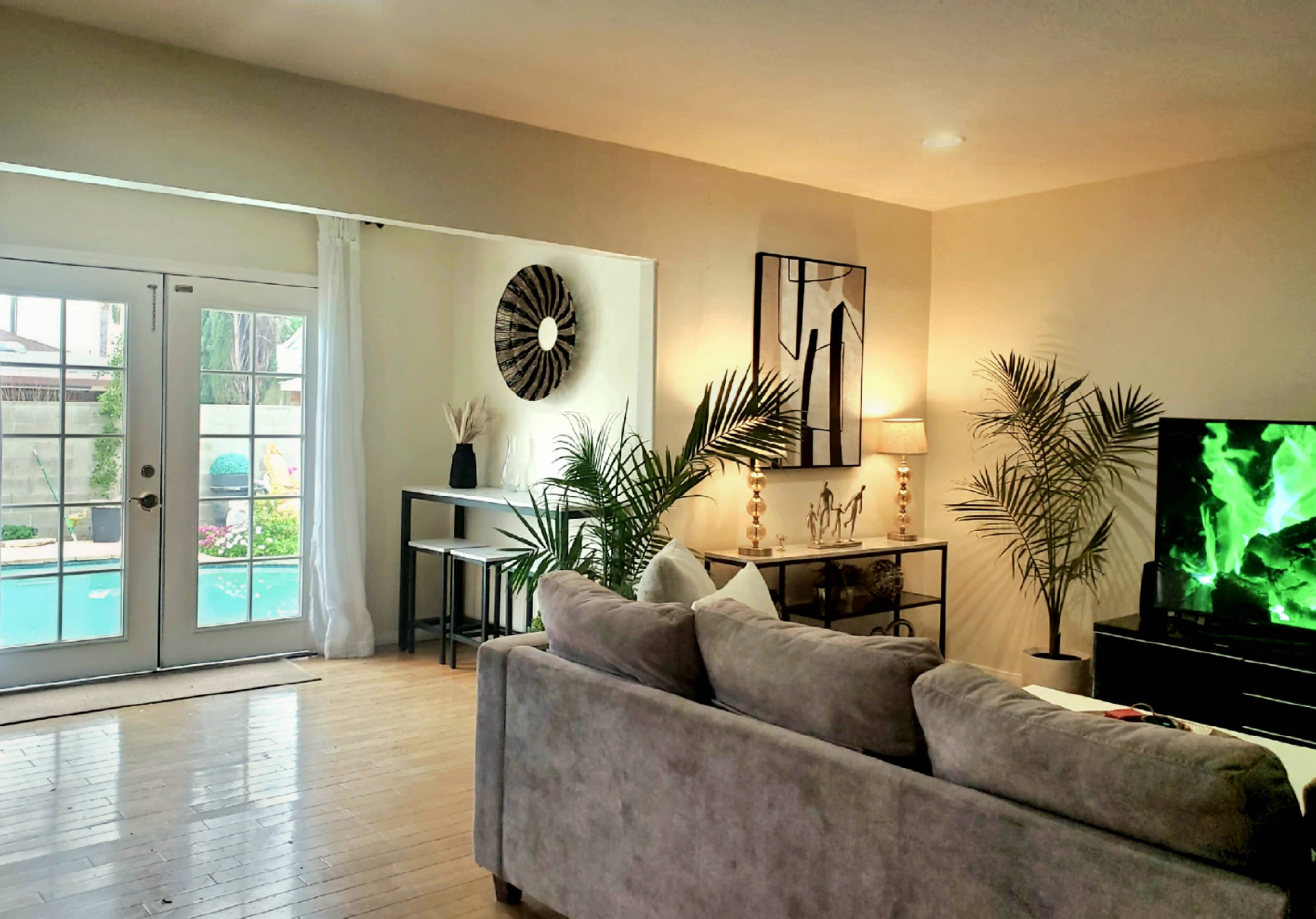 A living room with a gray sofa, a television, and a view of a pool area through glass doors.