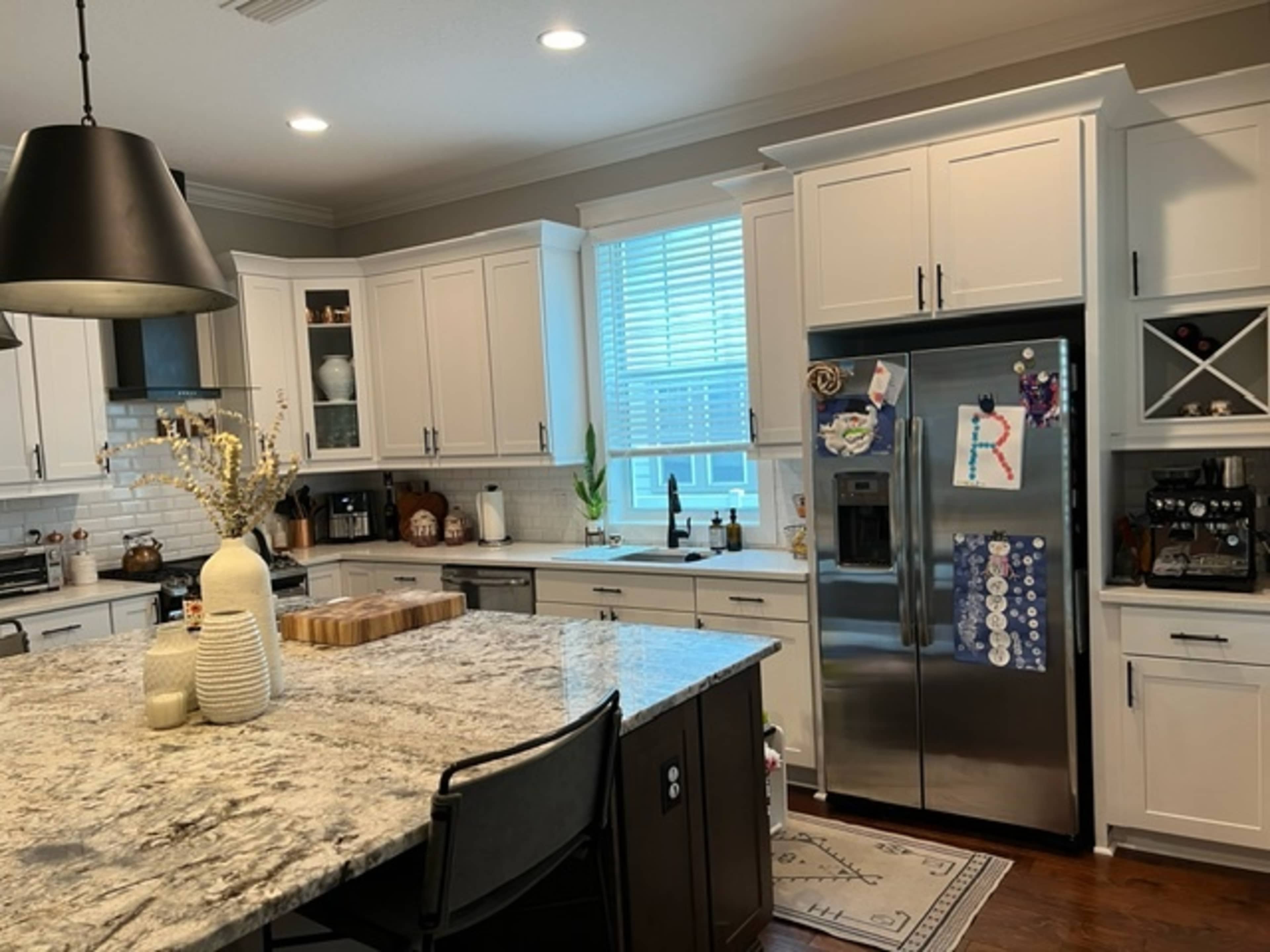 A modern kitchen featuring light-colored cabinets, a large granite island, and stainless steel appliances, with a window above the sink.