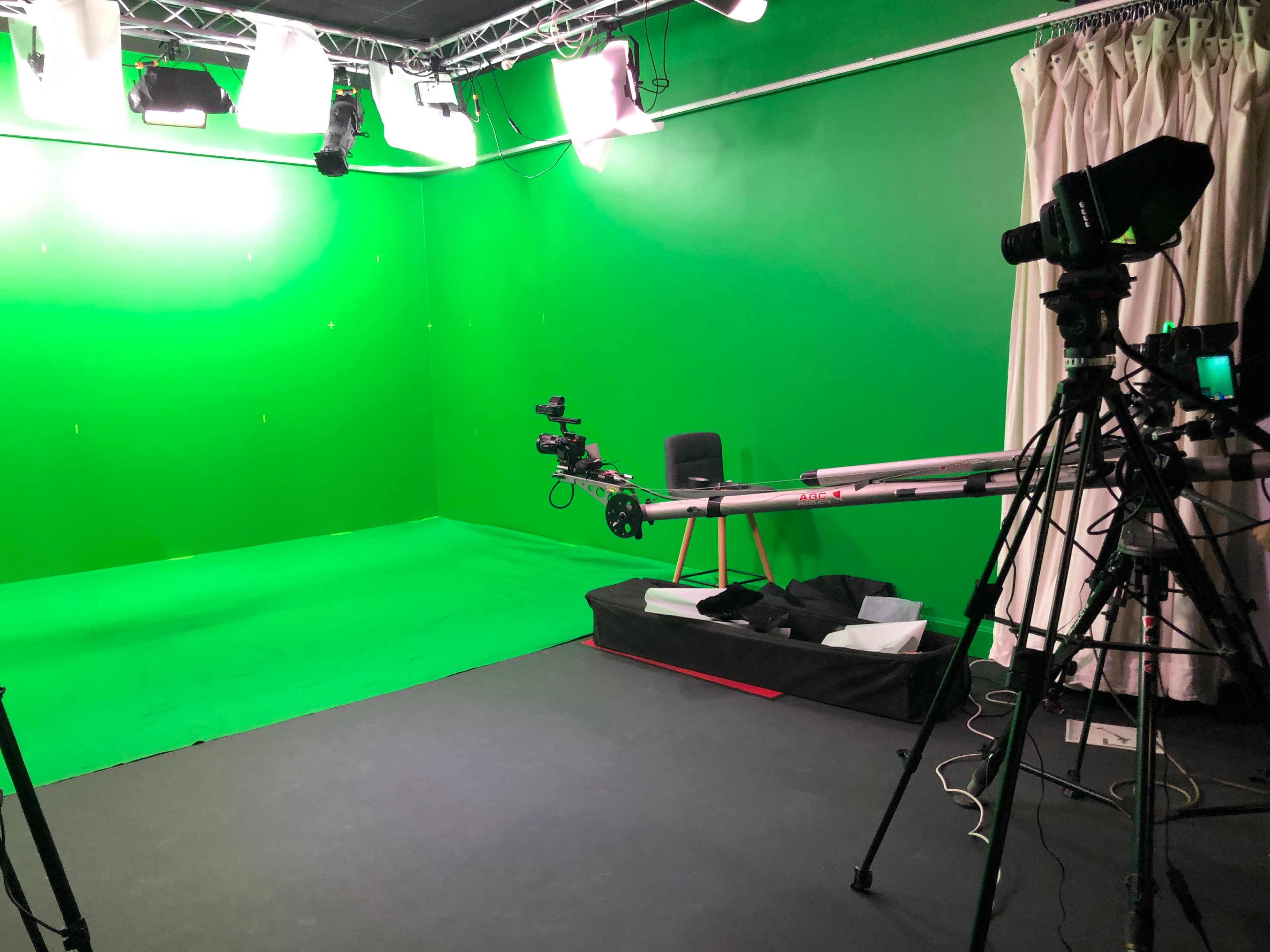 A green screen studio setup with a camera on a tripod, a camera dolly, and studio lighting equipment.