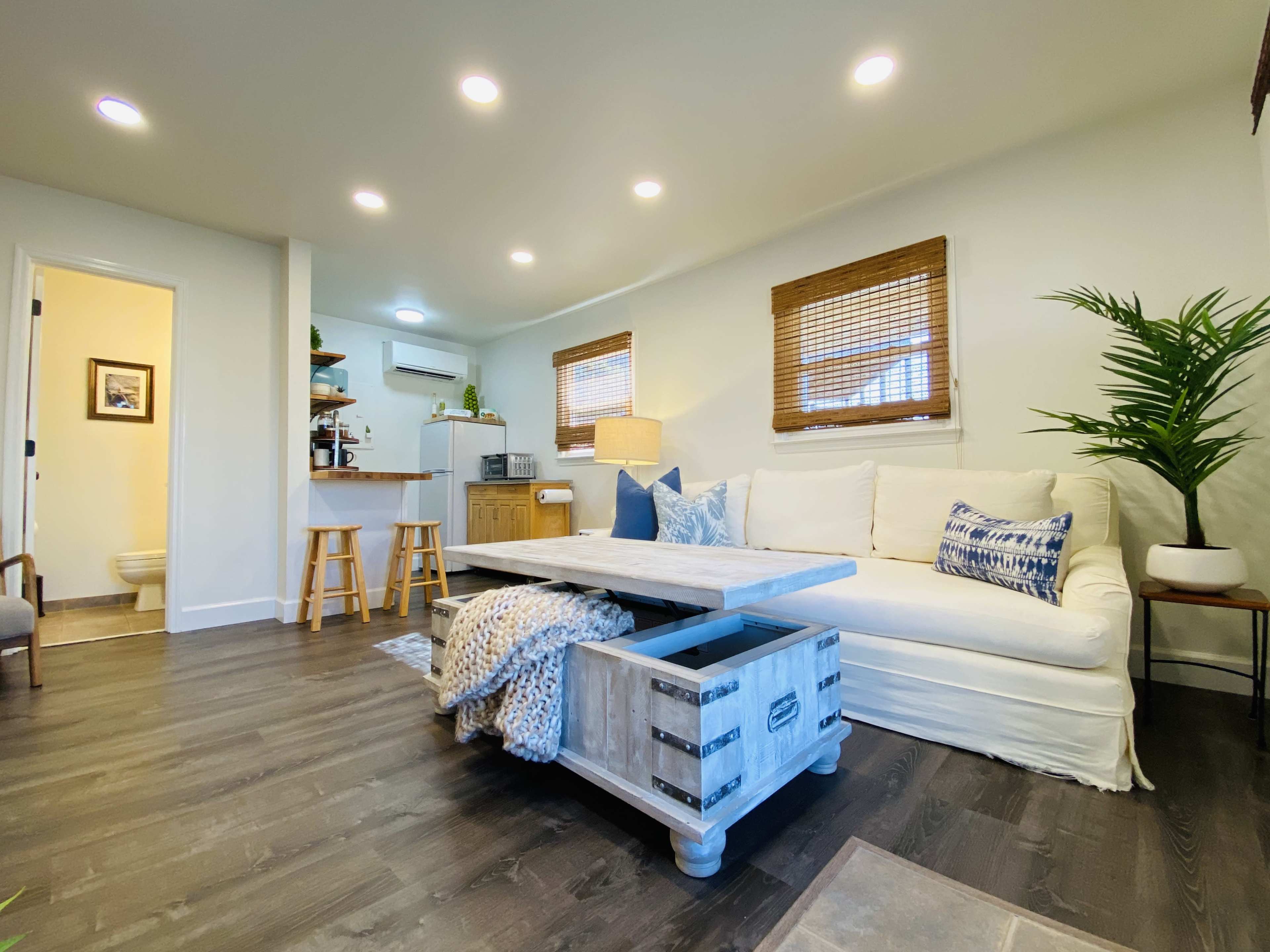 A modern living room with a white sofa, a coffee table, and a kitchen area in the background.