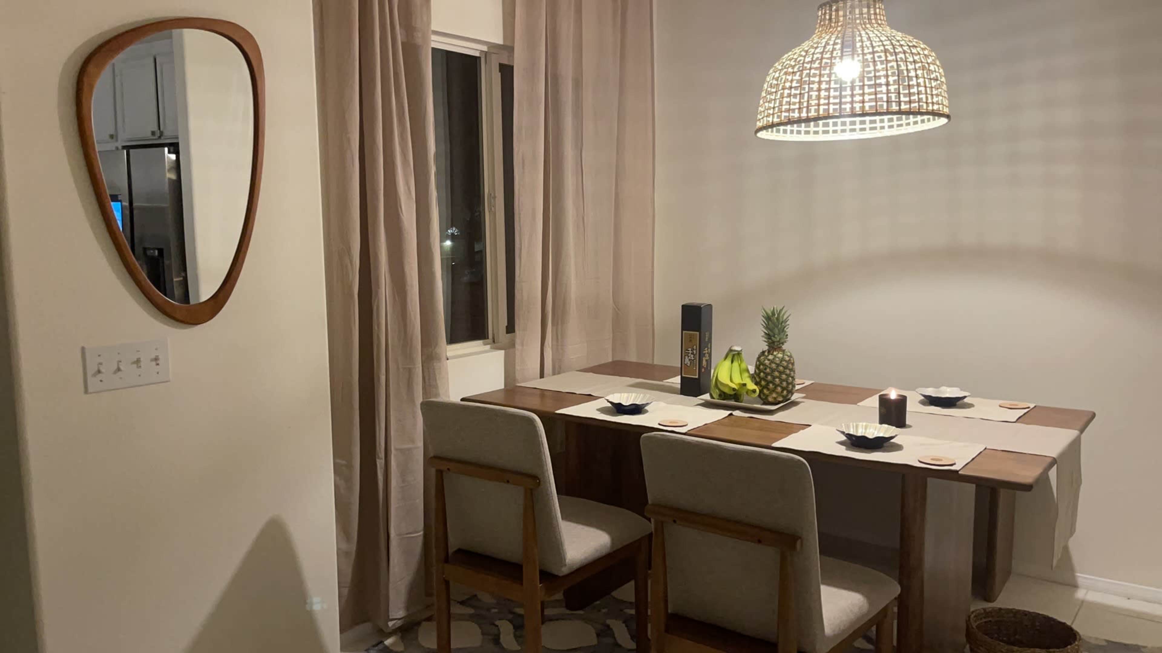 A dining area features a wooden table with four chairs, a mirror on the wall, and a pendant light overhead.