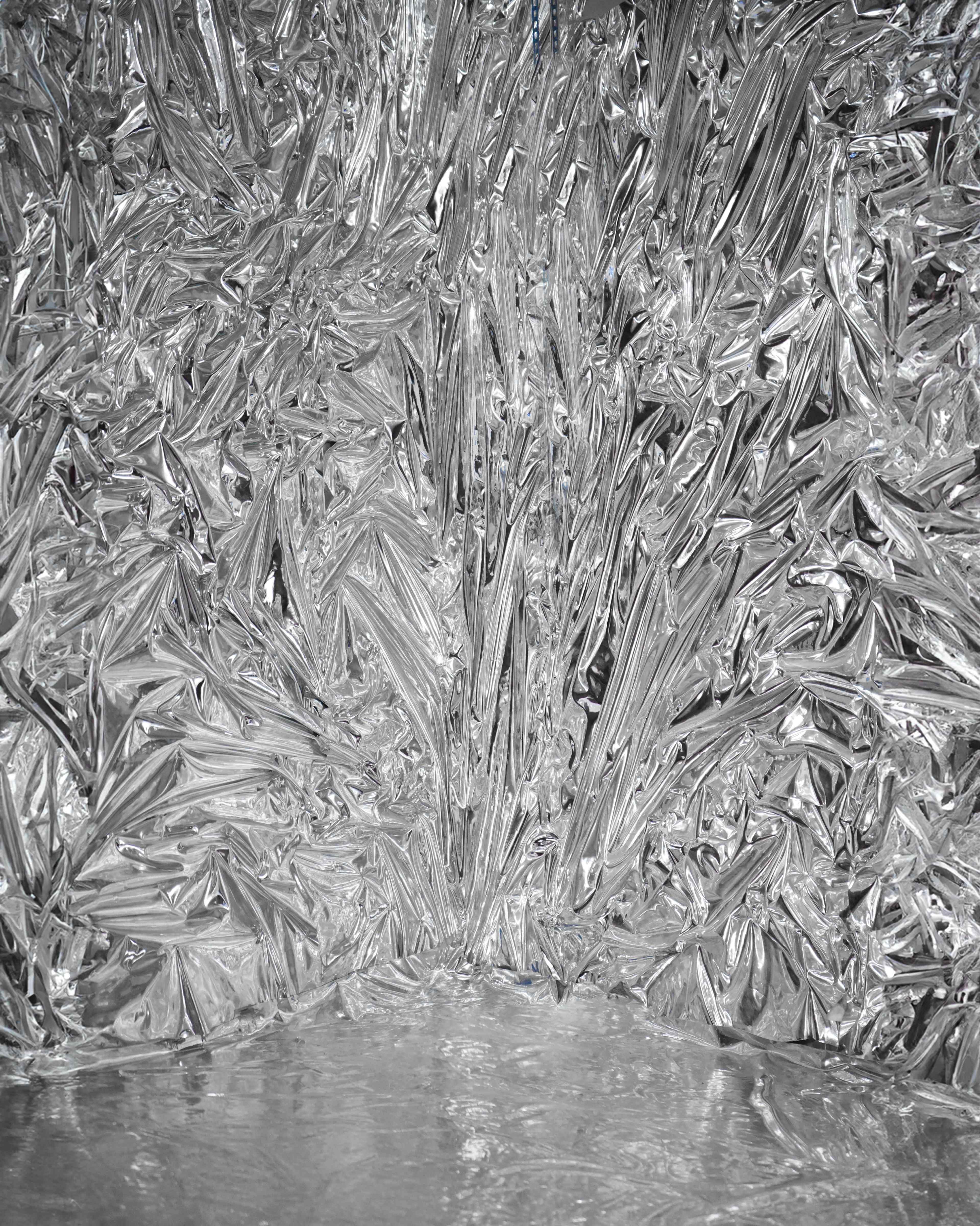 The image features a crumpled, shiny silver foil texture that creates a reflective surface and intricate patterns.