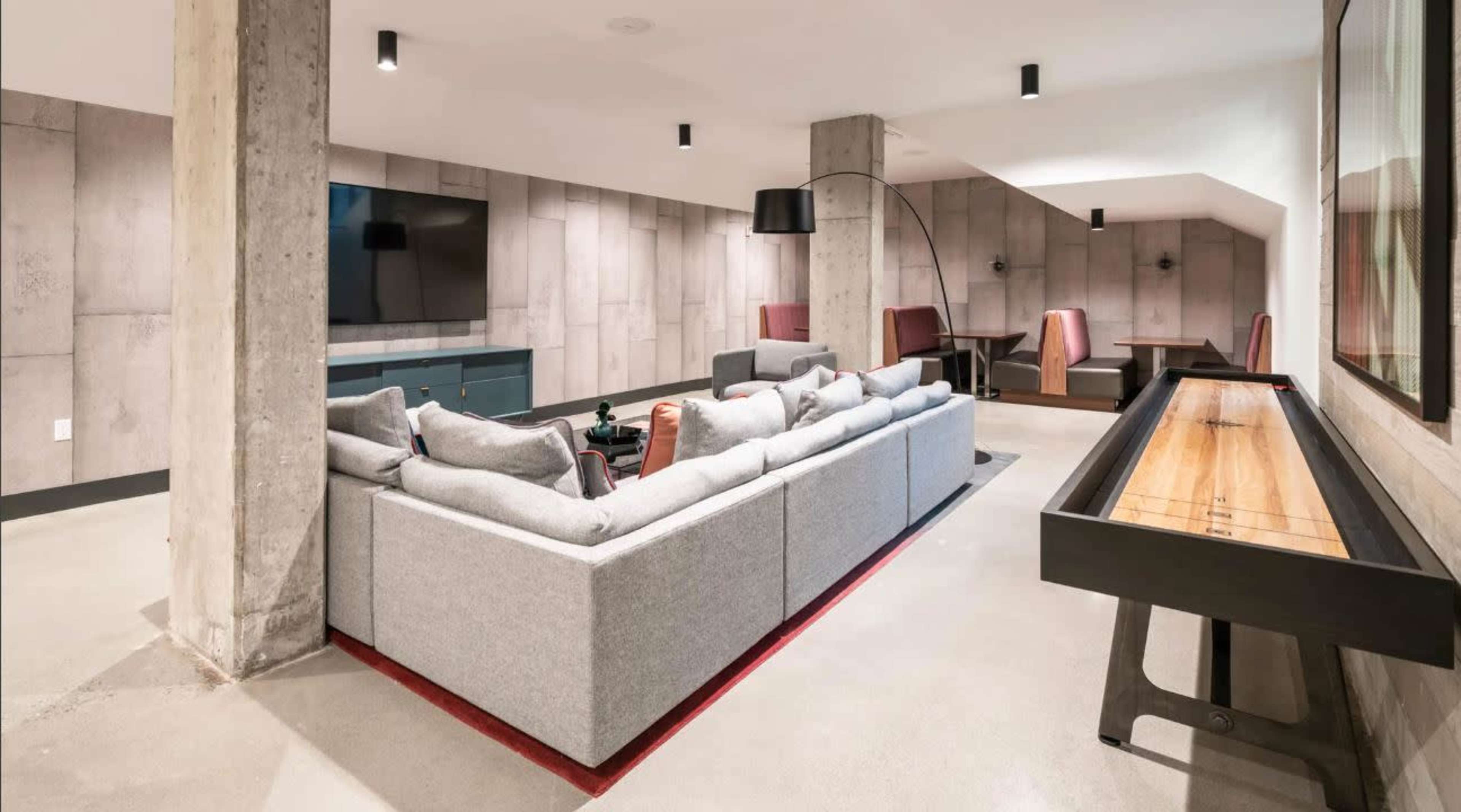 A modern, open-concept living space featuring a large sectional sofa, a television mounted on the wall, and a dining area with two high-backed chairs.