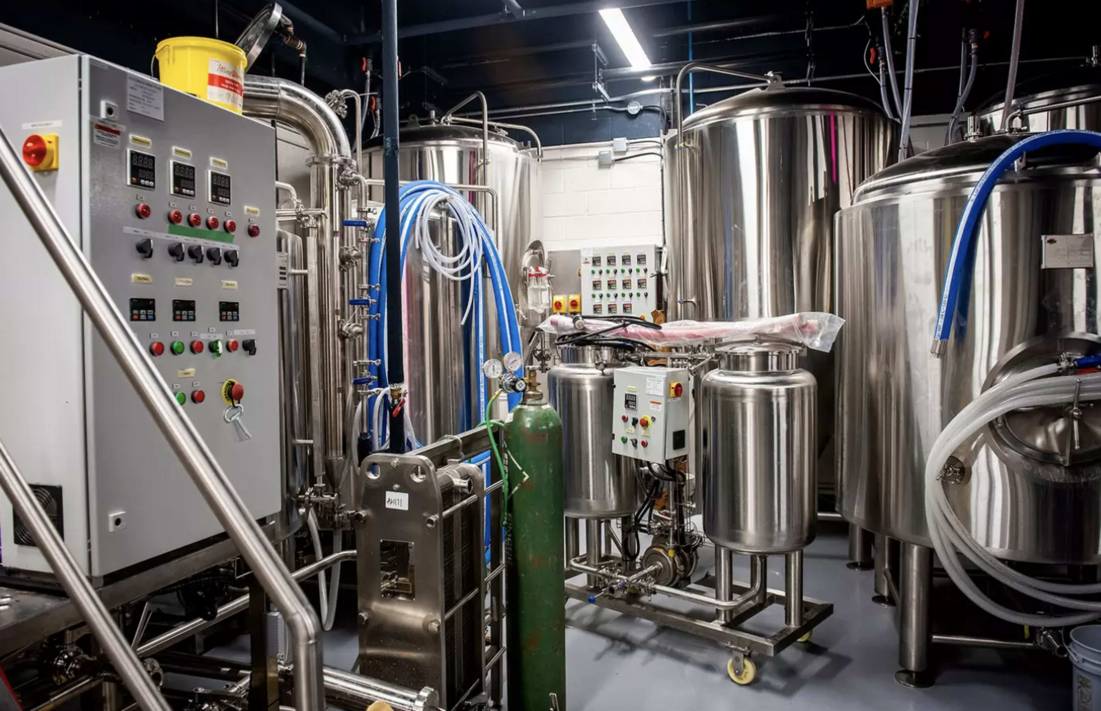 A brewing facility with several large stainless steel fermentation tanks and various control panels.