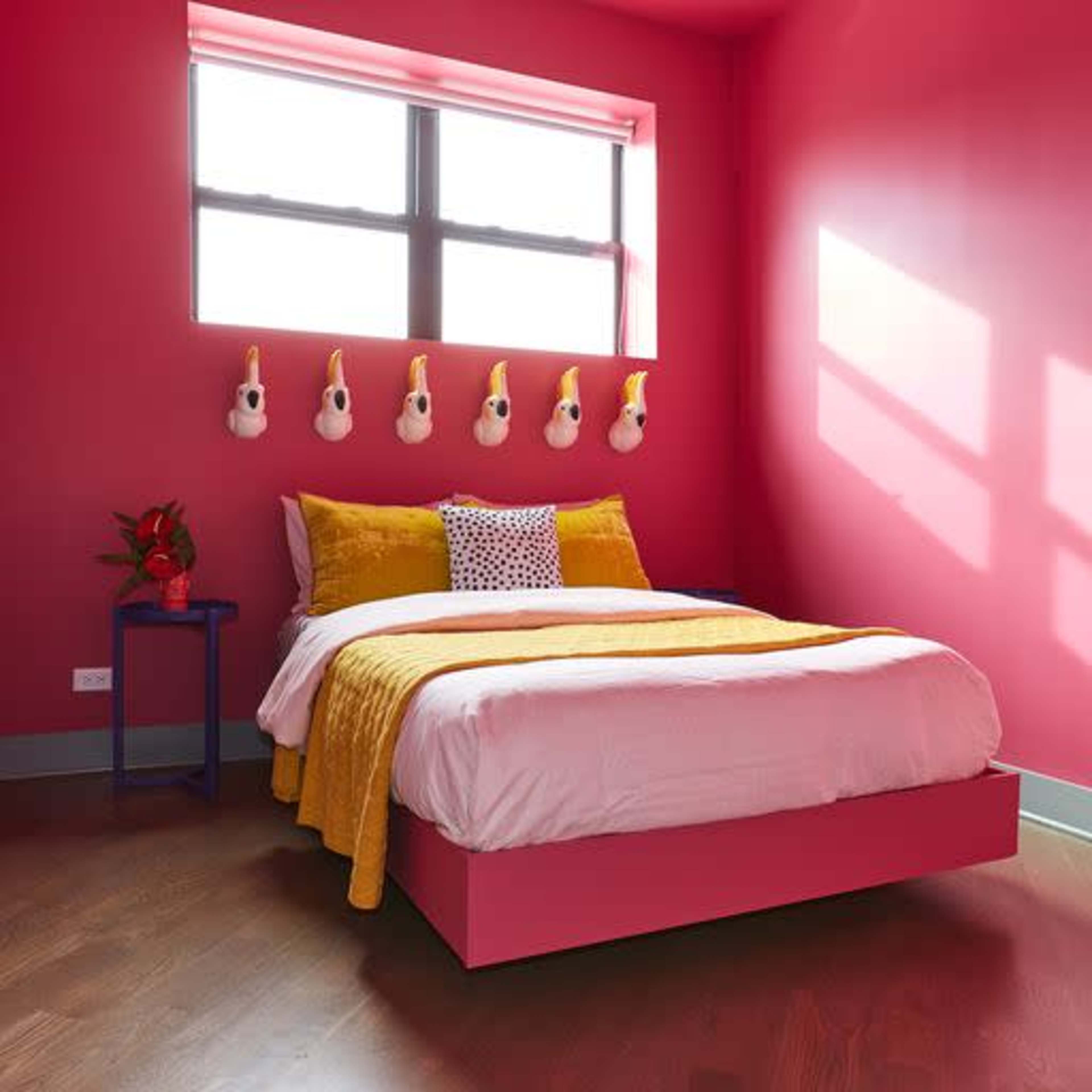 A brightly colored bedroom features a pink accent wall, a white bed with a yellow blanket, and decorative wall hooks.