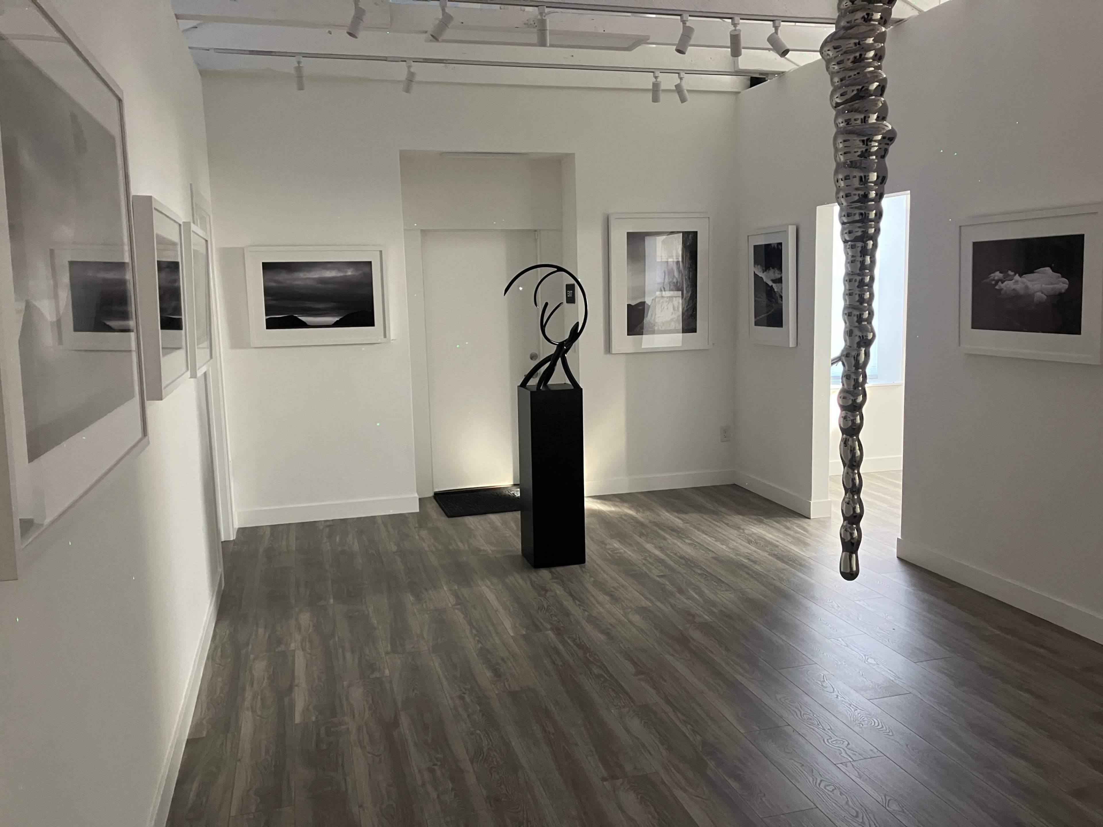 A minimalist art gallery featuring black and white photographs on the walls and a sculpture displayed on a pedestal in the center.