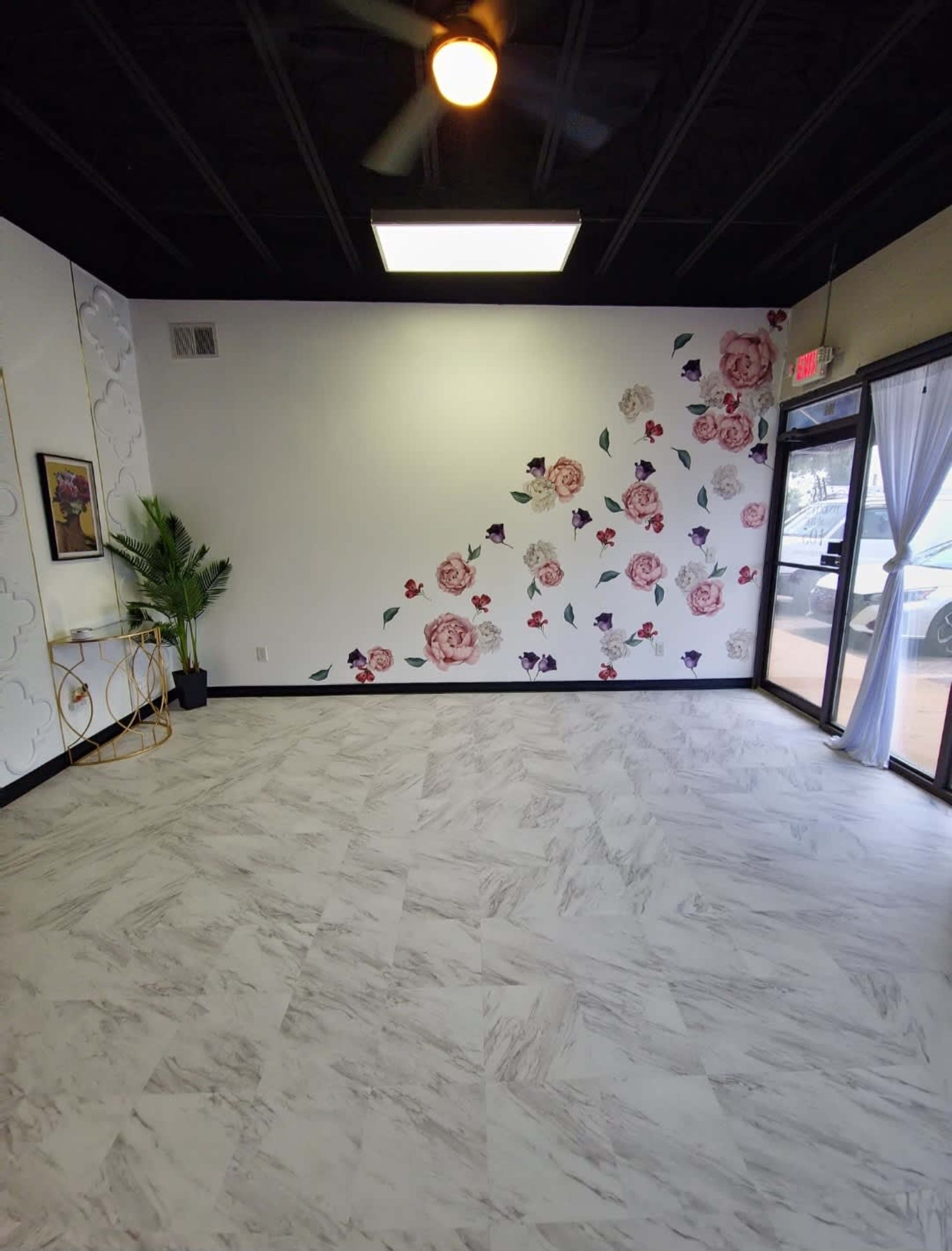A sparsely decorated interior room with a floral accent wall and large windows allowing natural light to enter.